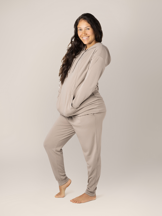 Pregnant model wearing the Bamboo Nursing Hoodie in Stone Taupe with her hands in her pockets. @model_info:Desiree is wearing a Small.