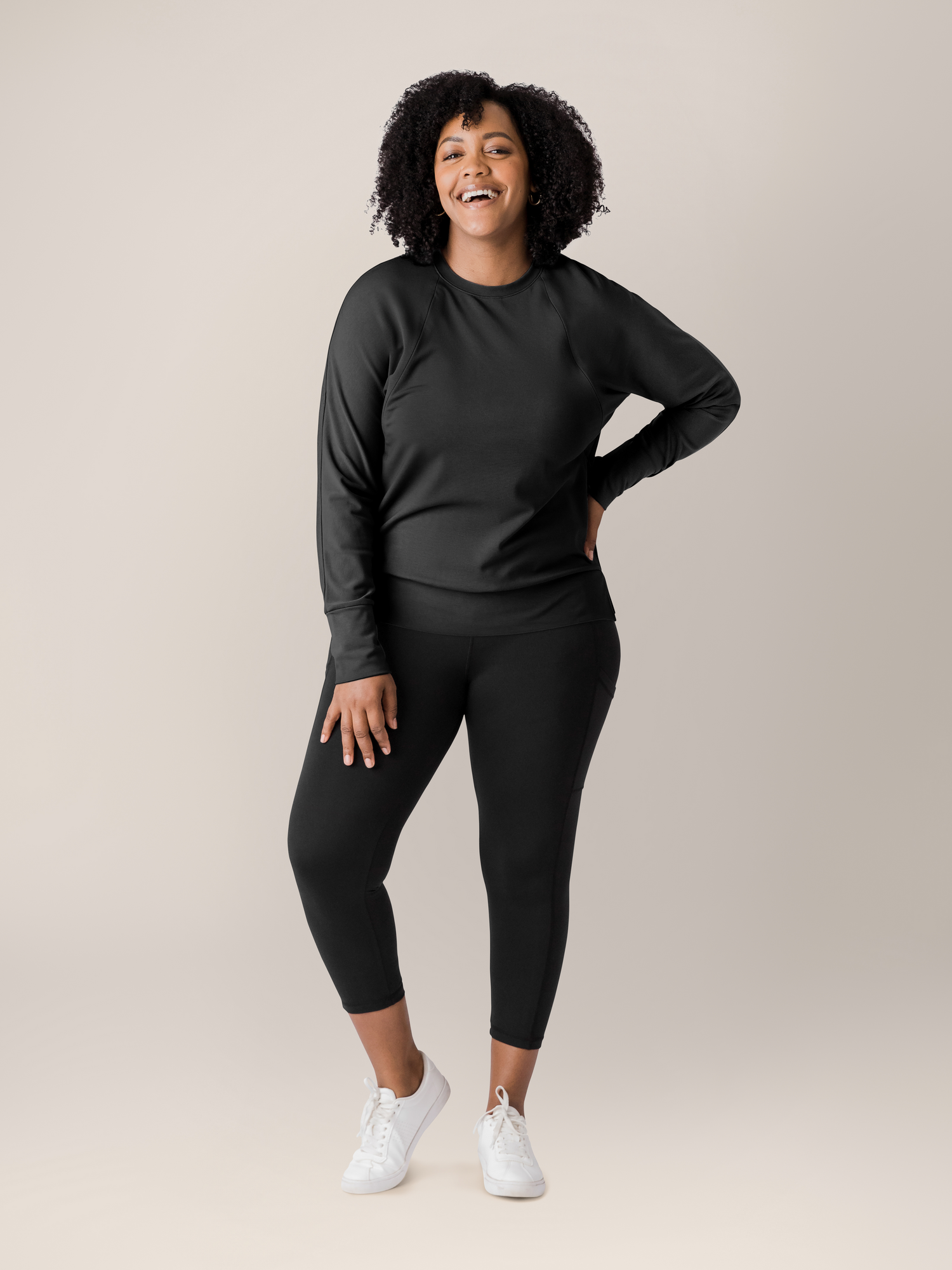 Model wearing the Bamboo Maternity & Nursing Crew Neck Sweatshirt in Black with her hand on her lag @model_info:Roxanne is wearing a Large.