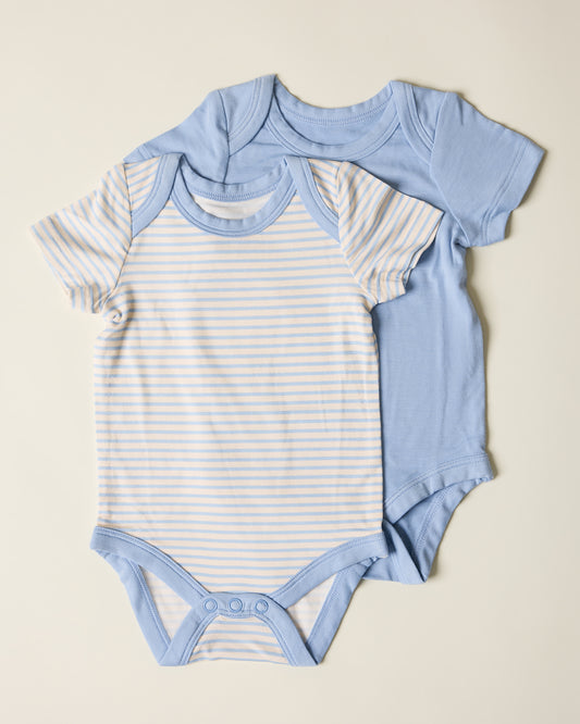 Two baby bodysuits, one with blue striped pattern and on solid blue on a beige background