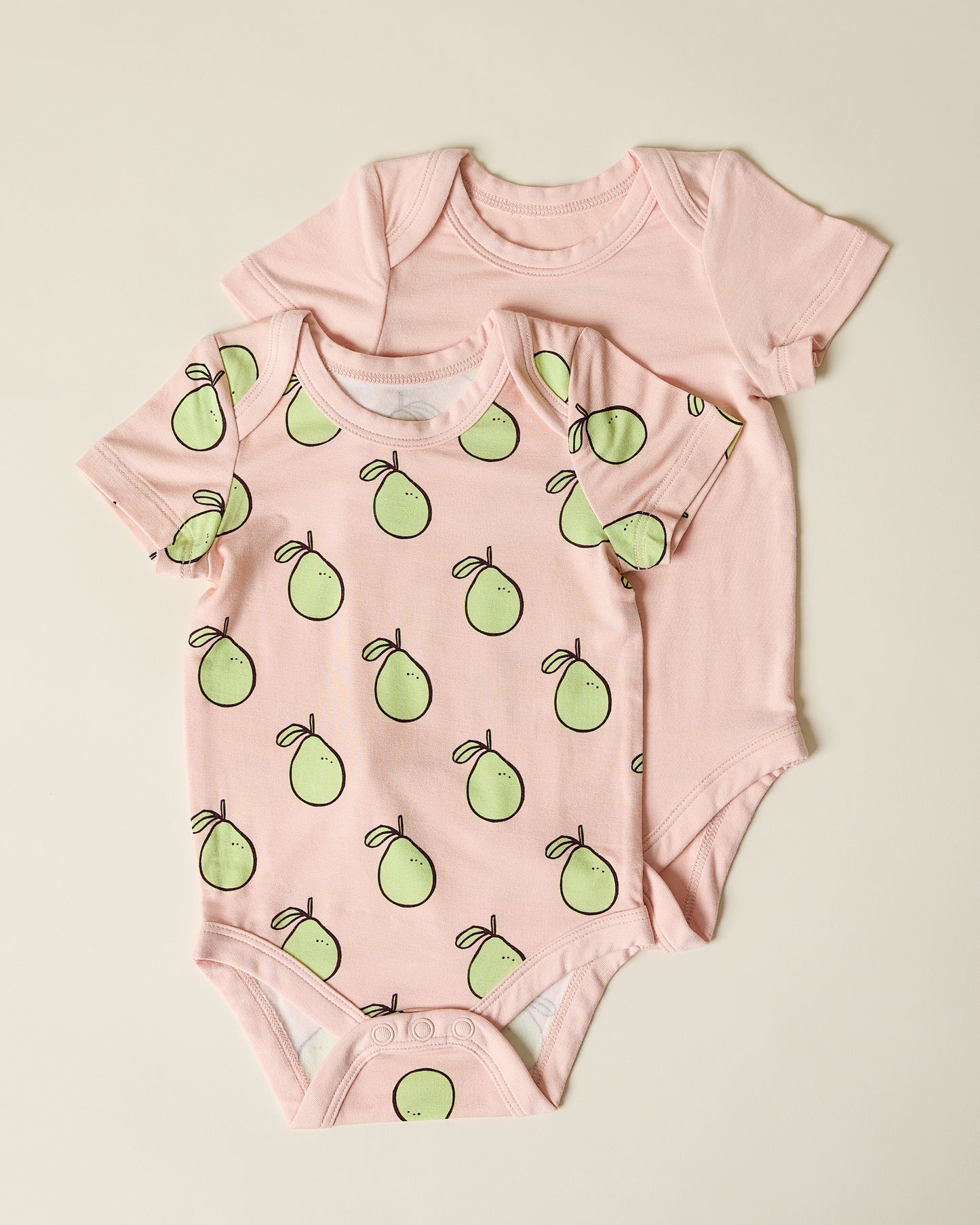 Two pink baby bodysuits, one with green pomelo pattern on a beige background