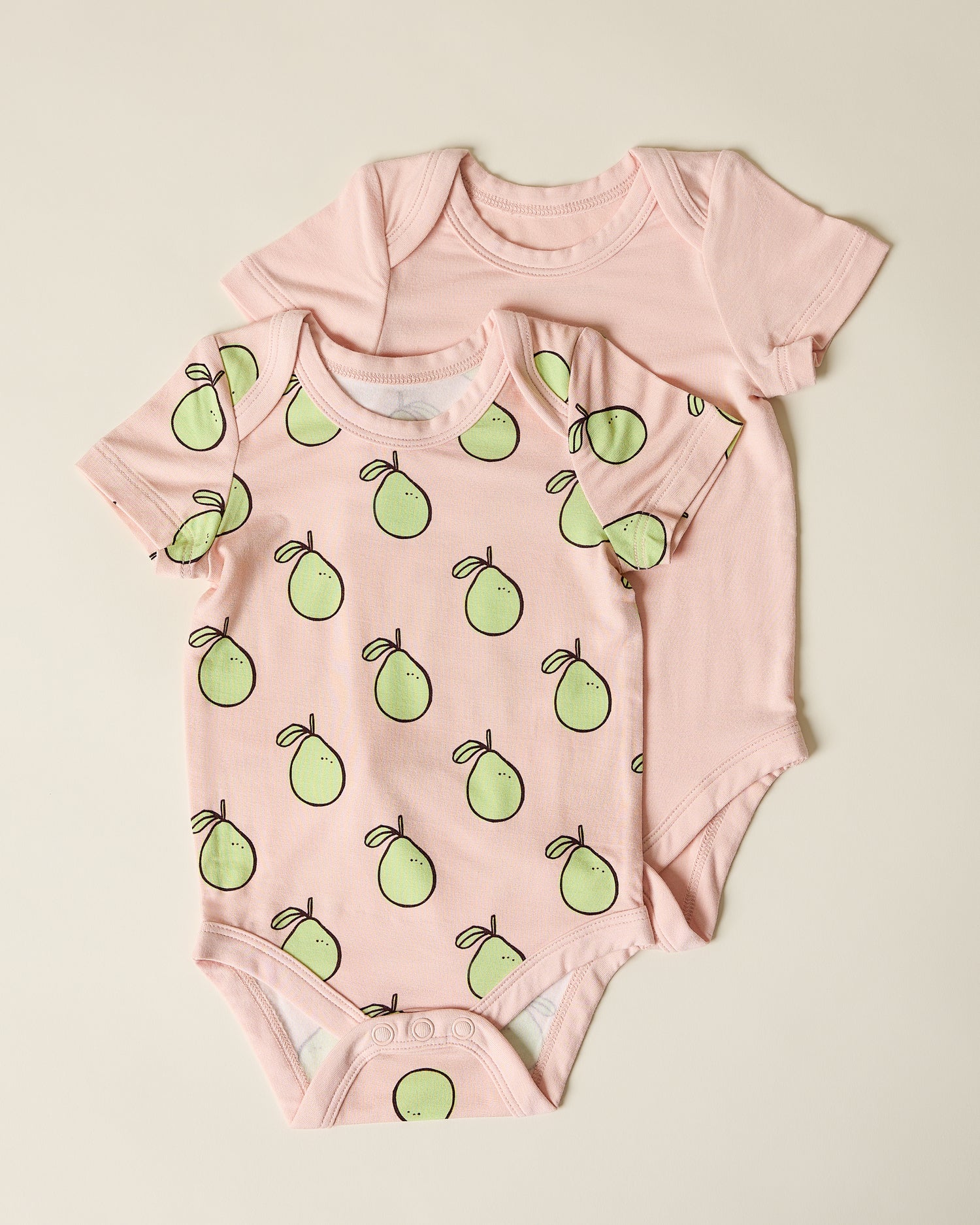Two pink baby bodysuits, one with green pomelo pattern on a beige background