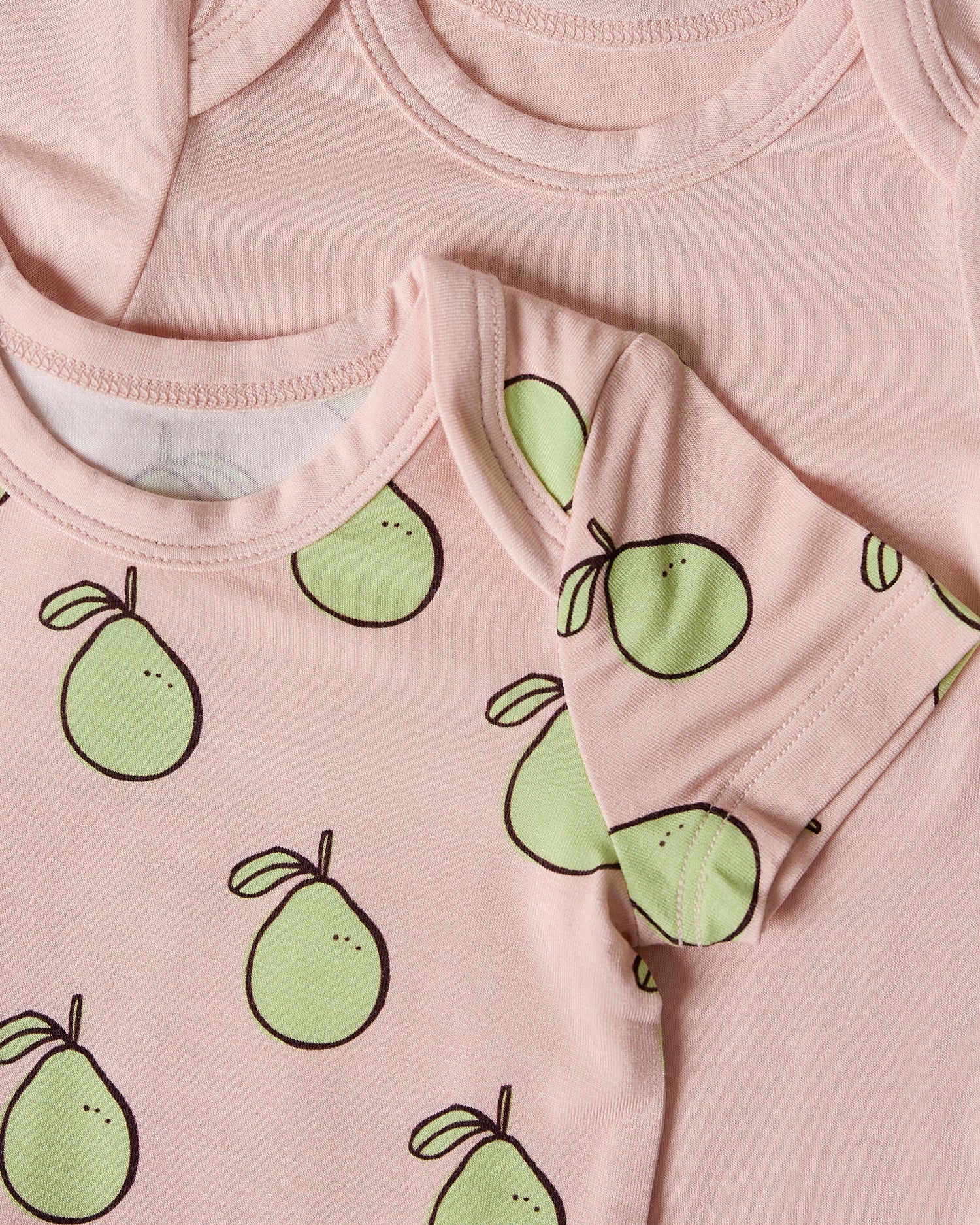 Close-up of two pink baby onesies, one with green pomelo patterns