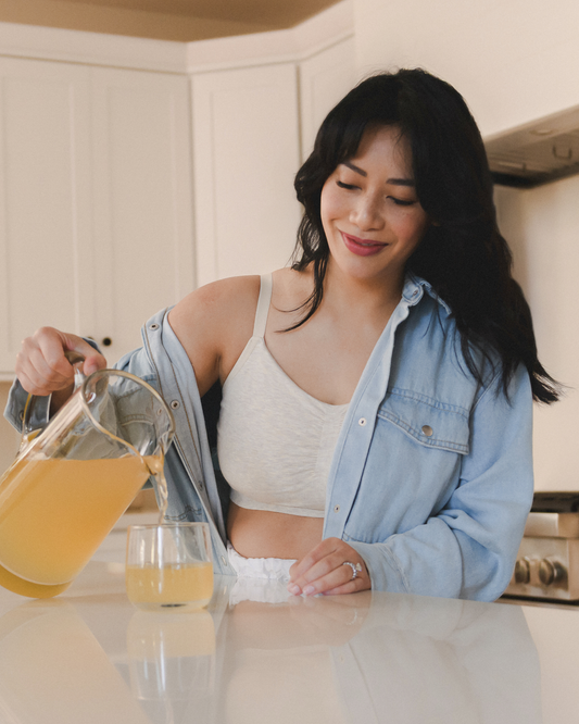 Model pouring juice while wearing the Sublime Hands-Free Pumping & Nursing Sleep and Lounge Bra in Oatmeal Heather @model_info:Nikki is wearing a Medium.