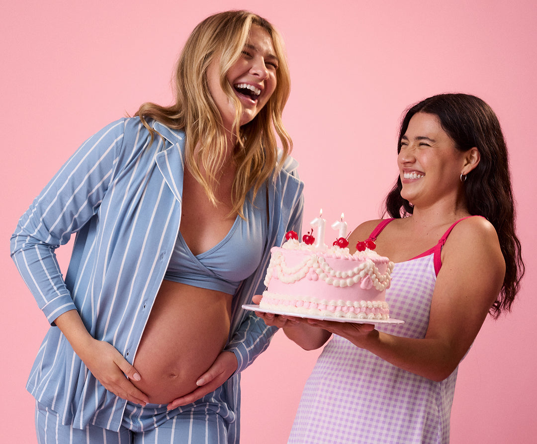 Two women celebrating with a cake against a pink background