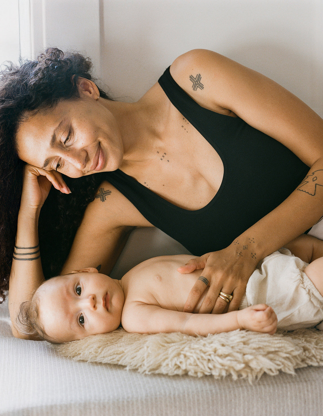 Model wearing the Sublime® Bamboo Scoop Neck Maternity & Nursing Longline Bra Top in Black, laying down with baby