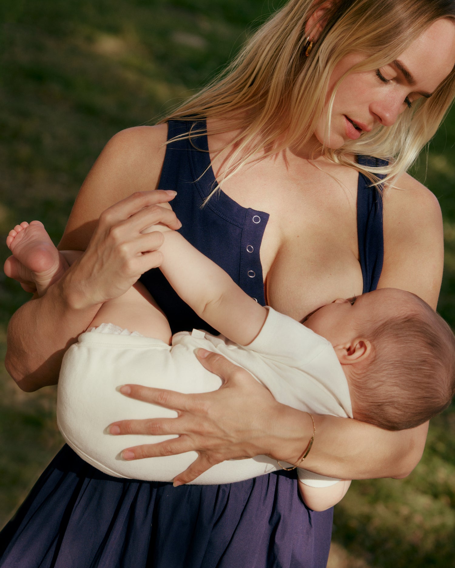 Woman breastfeeding a baby outdoors wearing the Charlotte Mixed Media Nursing Midi Dress in navy @model_info:Anni is 5'5" and wearing a Small.
