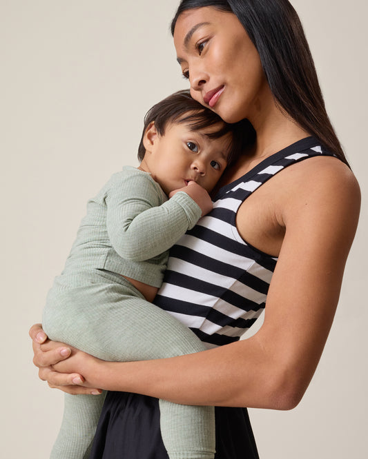 Woman wearing the Charlotte Mixed Media Nursing Midi Dress with black & white striped top and black skirt, holding a child against a beige background