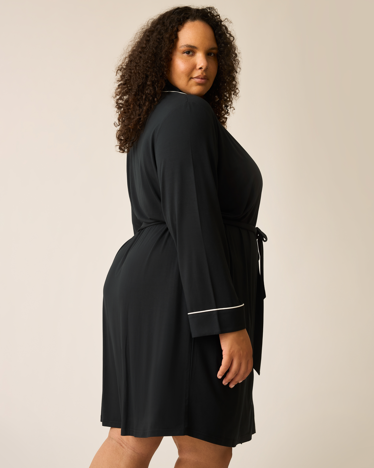 Woman wearing the Clea Bamboo Robe in black with white trim on a beige background