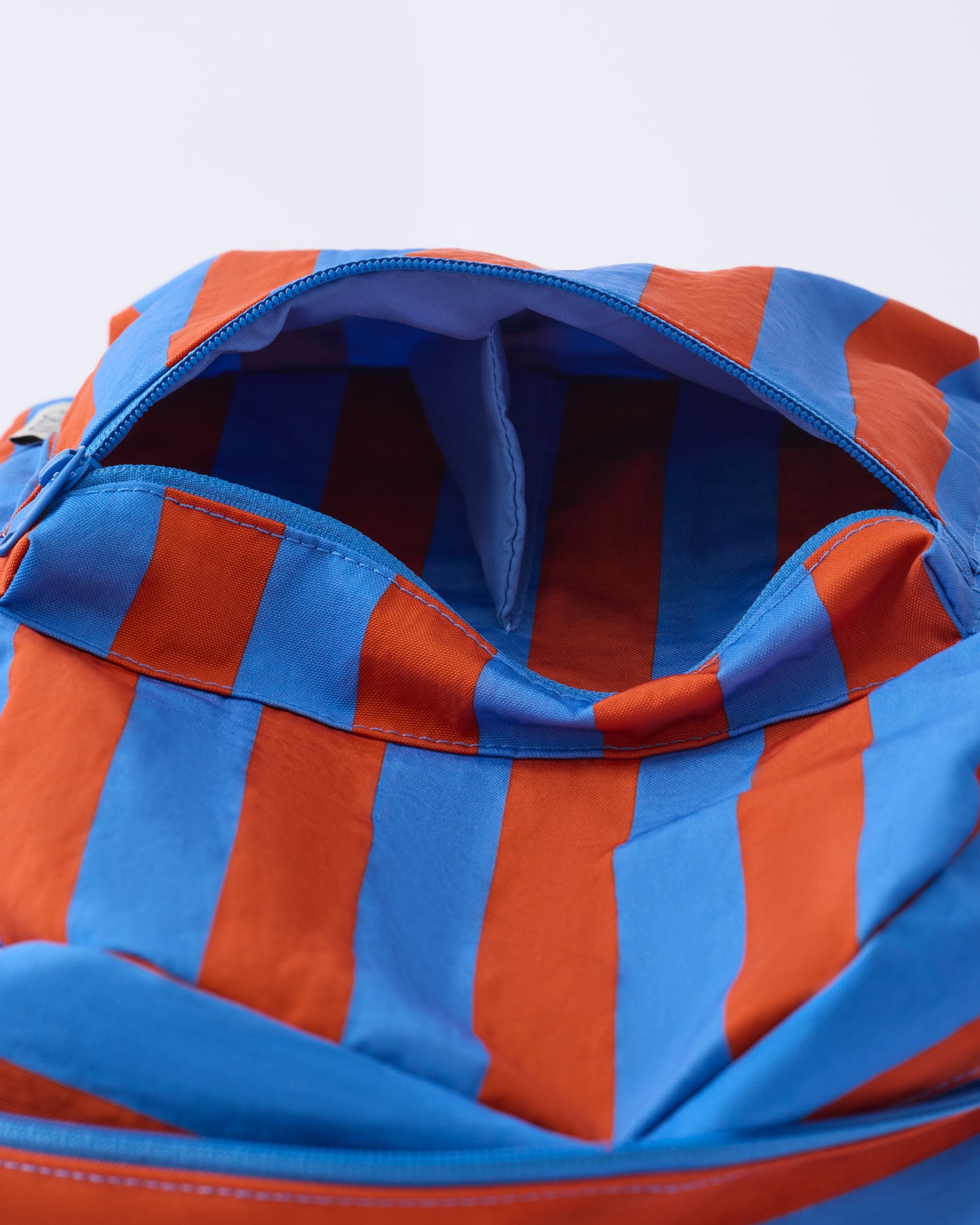 Close up of the zipper of the Cool Kid Backpack in Blue & Rust Stripe, on a beige background.