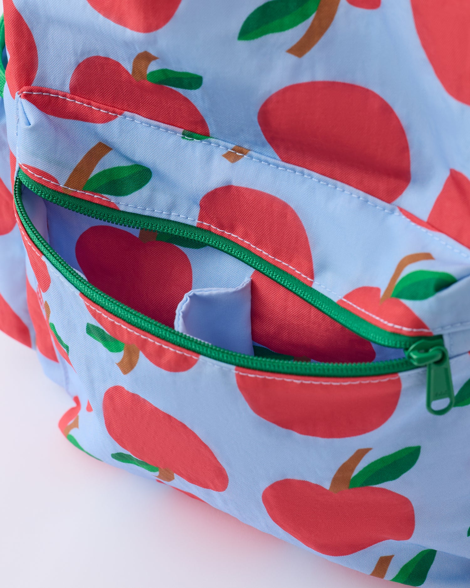 Close up of the front pocket zipper of the Cool Kid Backpack in Blue Apple on a beige background.