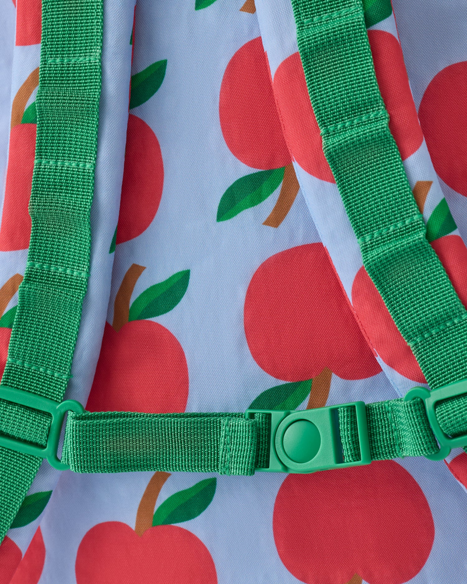 Close up of the shoulder strap clip of the Cool Kid Backpack in Blue Apple on a beige background.