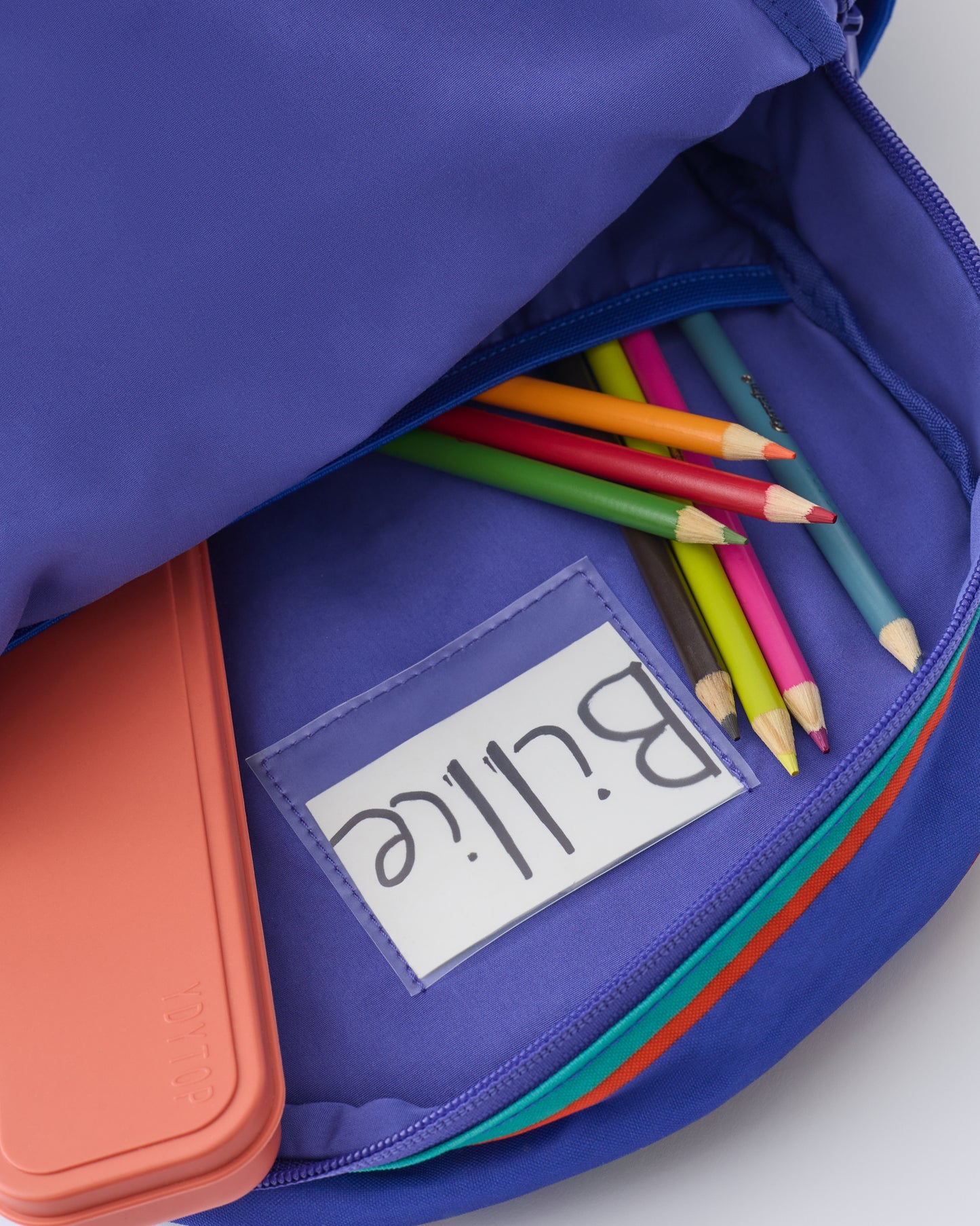 Inside view of Nametag, pocket and pencils inside the Cool Kid Backpack in Navy & Green Stripe on a beige background.