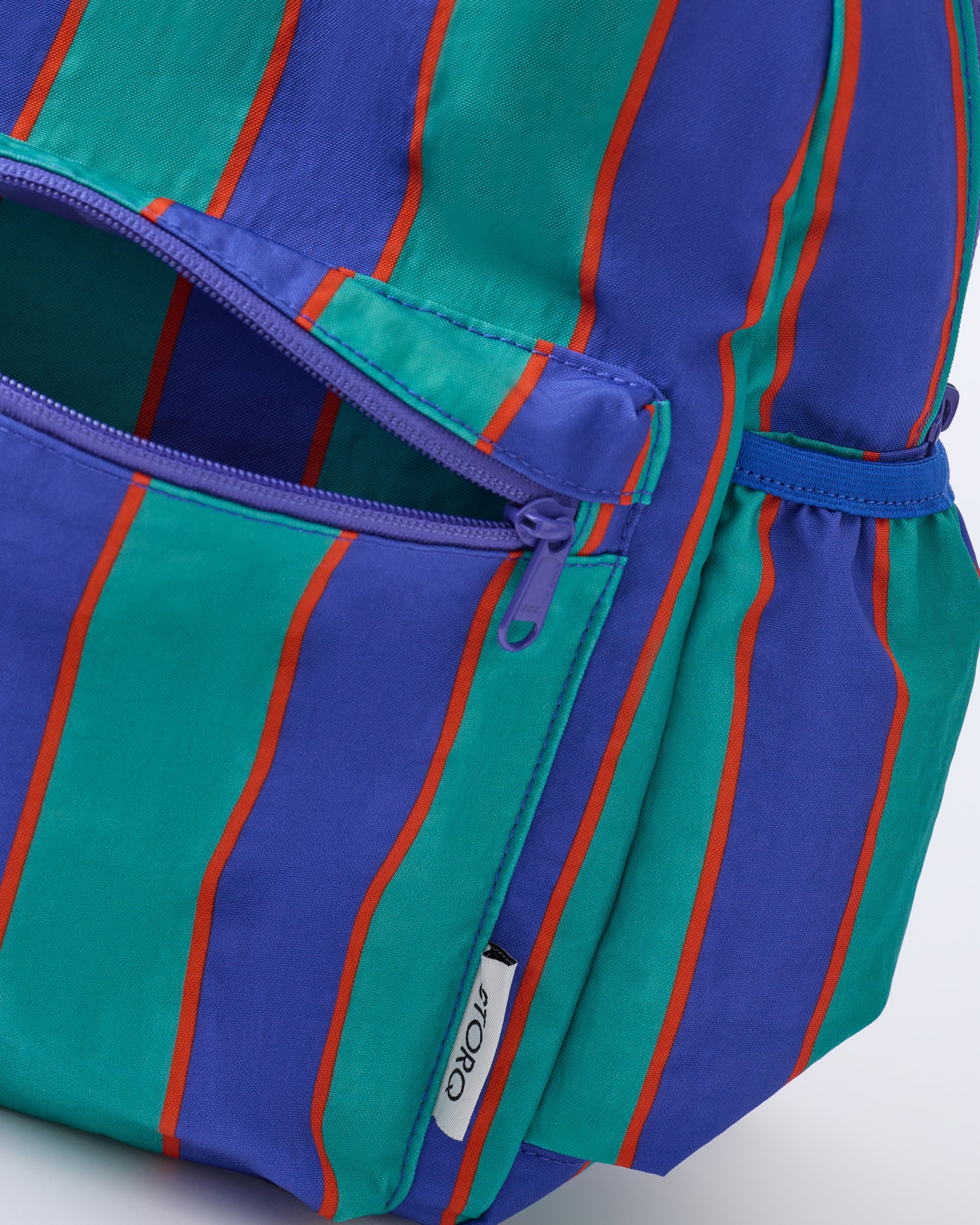 Close up of front pocket zipper of the Cool Kid Backpack in Navy & Green Stripe on a beige background.