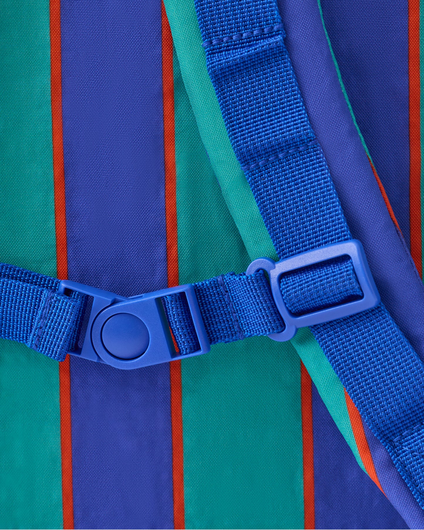 Close up of strap clip of the Cool Kid Backpack in Navy & Green Stripe on a beige background.