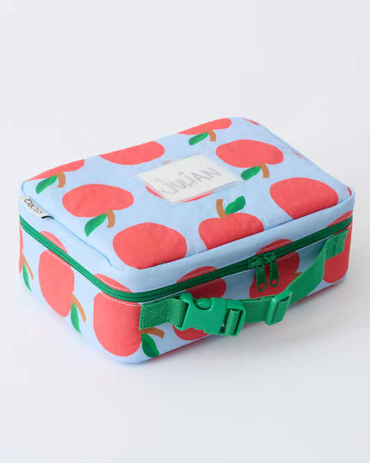 Angled view of Cool Kid Lunch Box in Blue Apple with name tag that reads Julian, on a beige background.