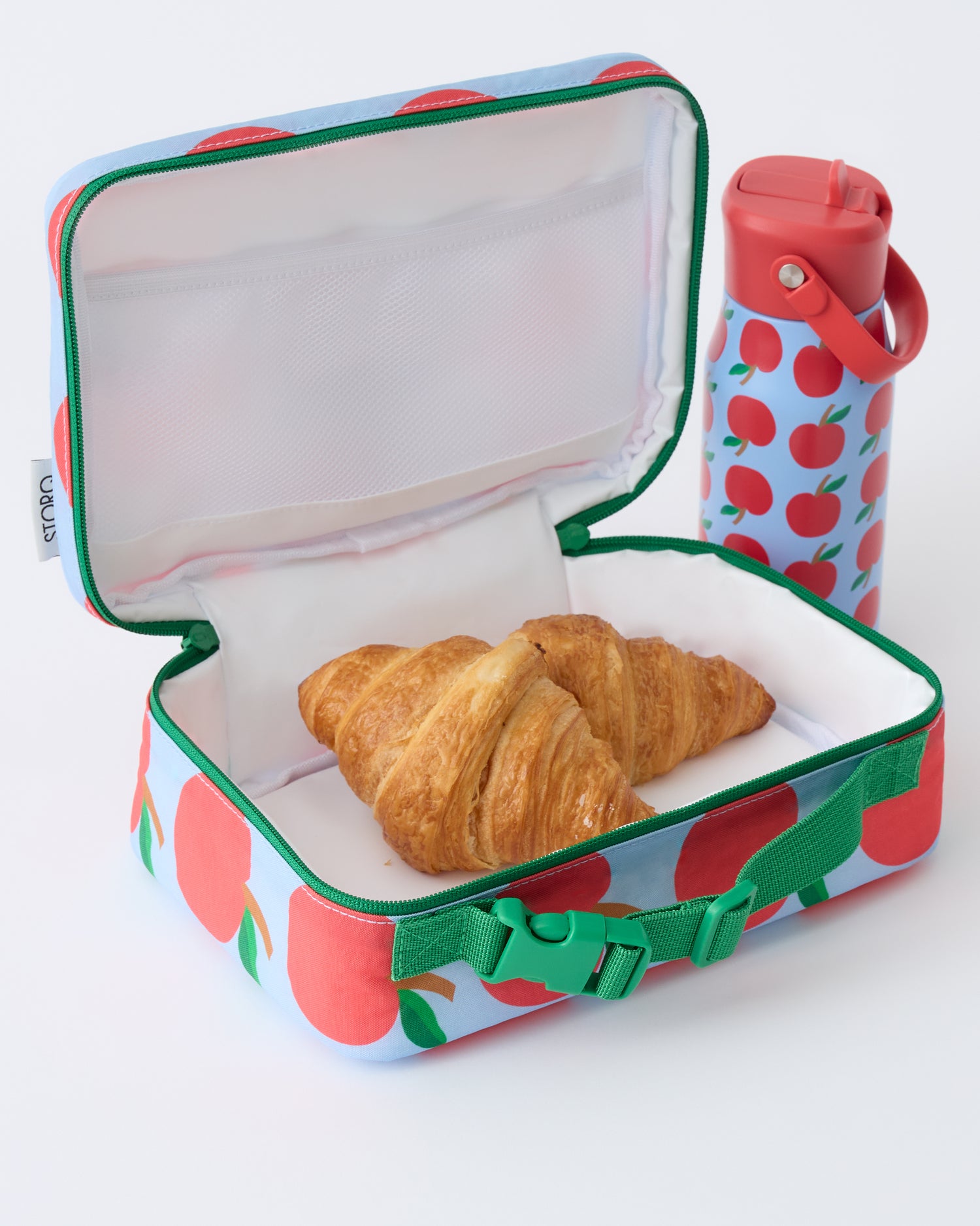 Cool Kid Lunch Box in Blue Apple is open with two croissants inside, next to Cool Kid Water Bottle in Blue Apple, on a beige background.