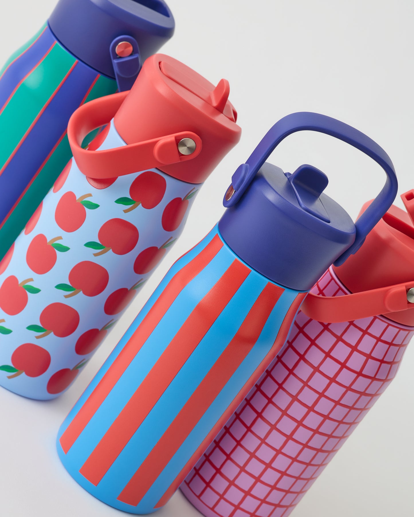 All four Cool Kid Water Bottles, in Orchid Grid, Blue Apple, Blue & Rust Stripe, and Navy & Green Stripe, on a beige background.