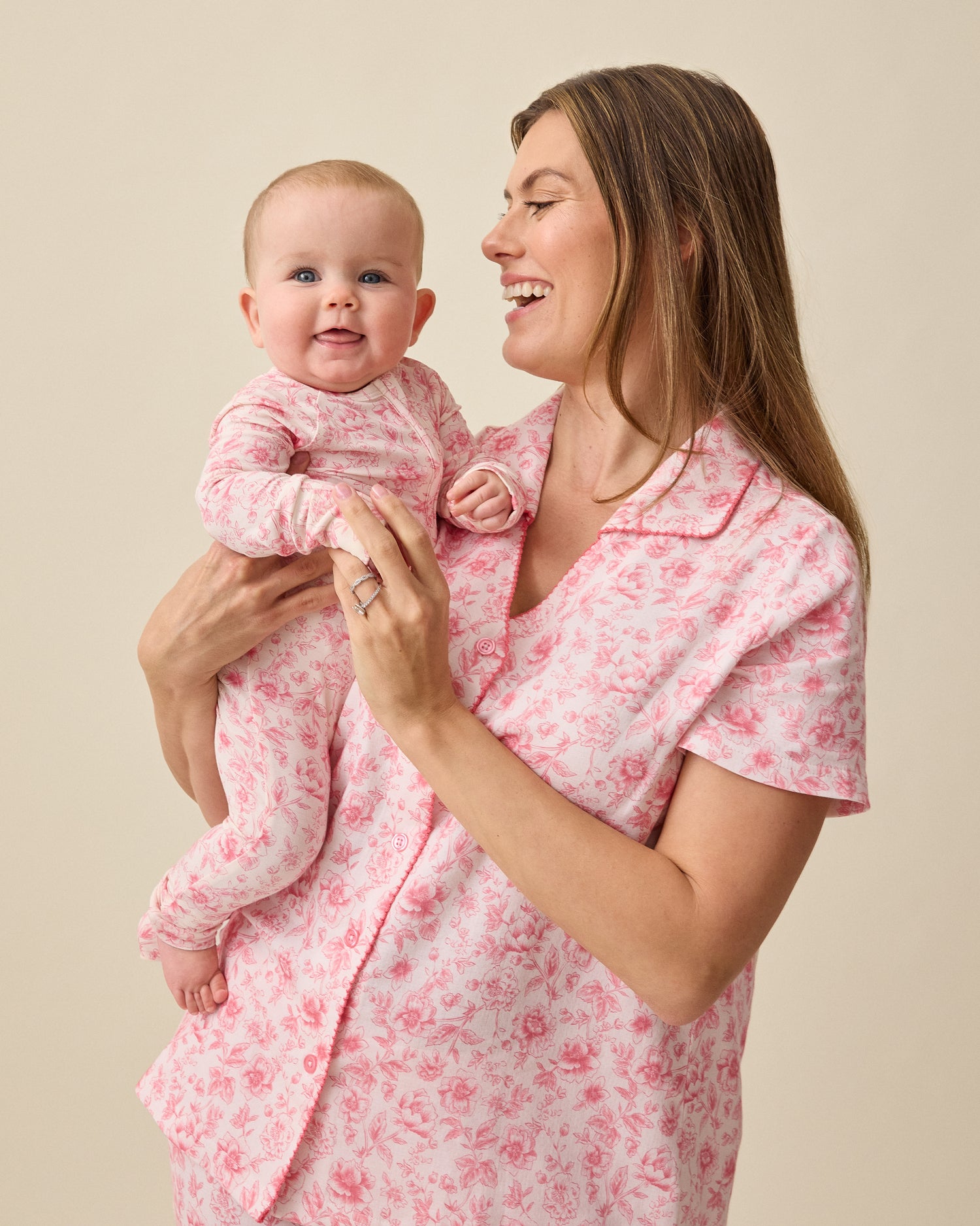 Woman holding baby and wearing Cotton Bamboo Pajama Set in Pink Toile on a beige background. Baby is wearing Bamboo Baby Pajama in Pink Toile.