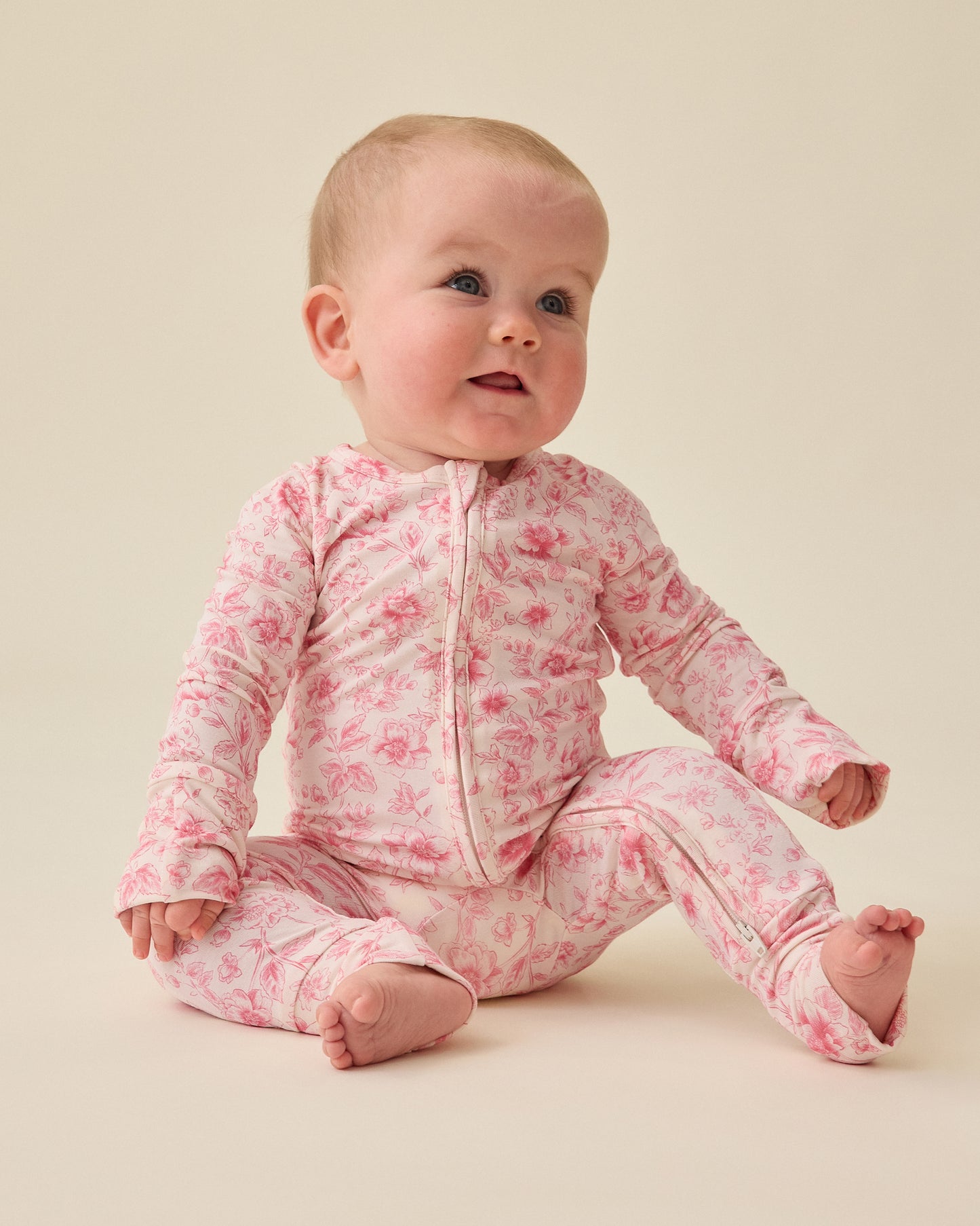 Baby sitting and wearing the Bamboo Baby Pajama in pink toile on a plain background@model_info:Charli is wearing 0-3 months.
