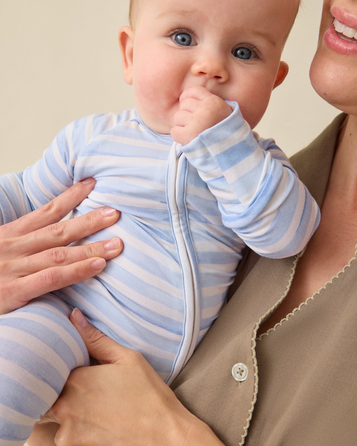 Baby wearing the Bamboo Baby Pajama in Blue Watercolor in woman's arms on a plan background