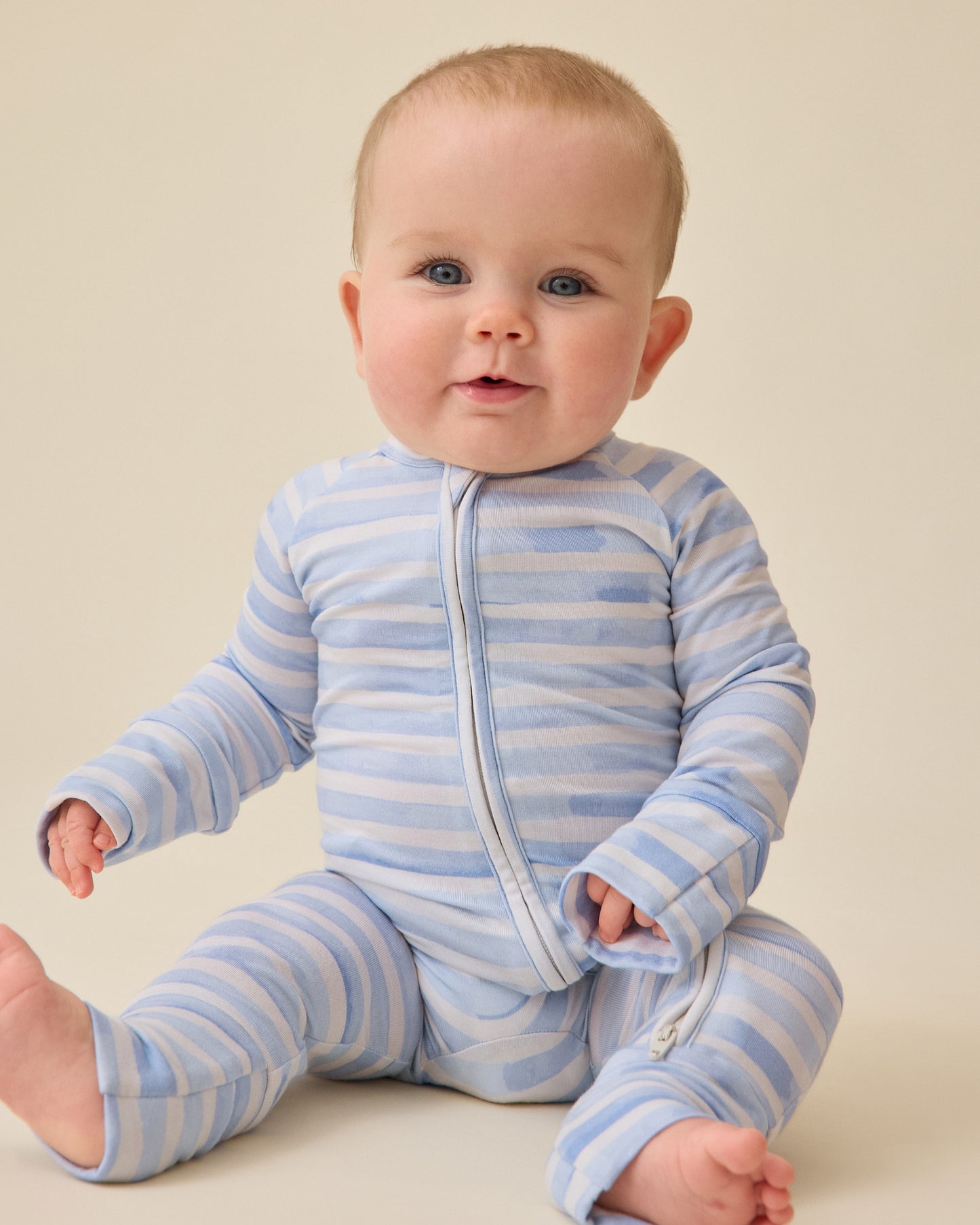Baby sitting and wearing the Bamboo Baby Pajama in Blue Watercolor on a plan background@model_info:Charli is wearing 0-3 months.