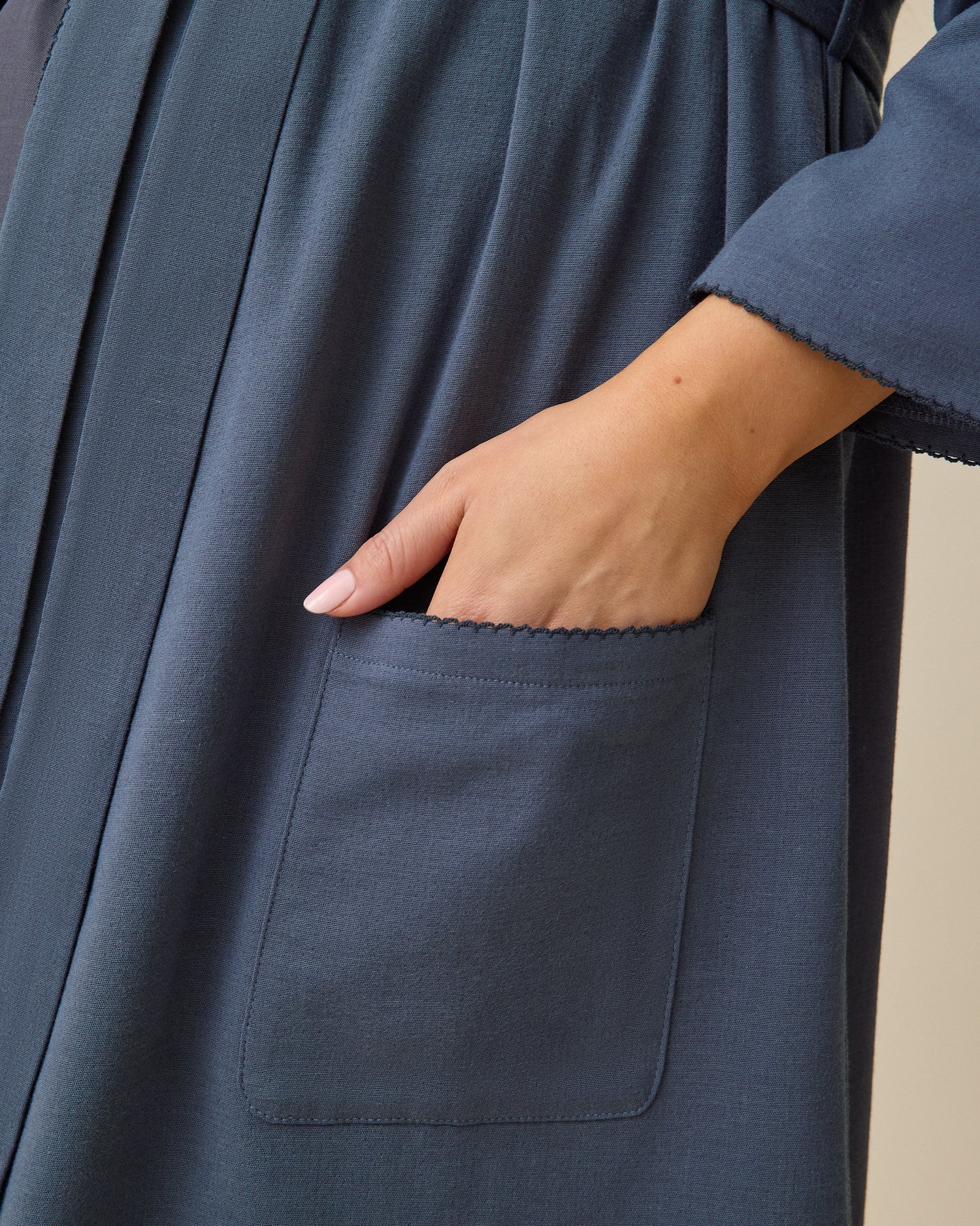 Model using pocket on Cotton Bamboo Robe in Midnight Blue on a beige background