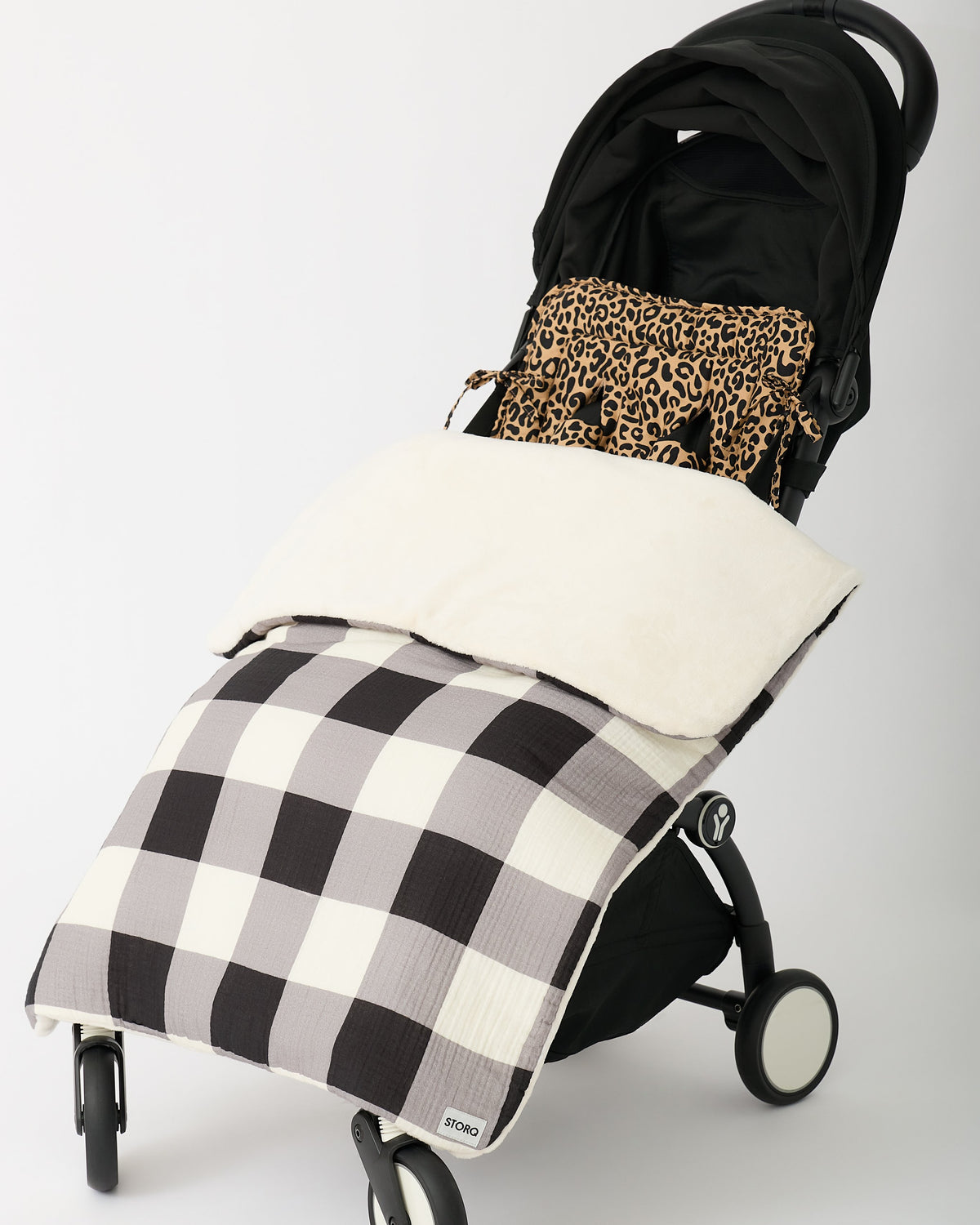 Black stroller with Stroller Party™ Seat Liner & Strap Covers in Leopard and Cozy Stroller Blanket in Buffalo Plaid, on an off white background.