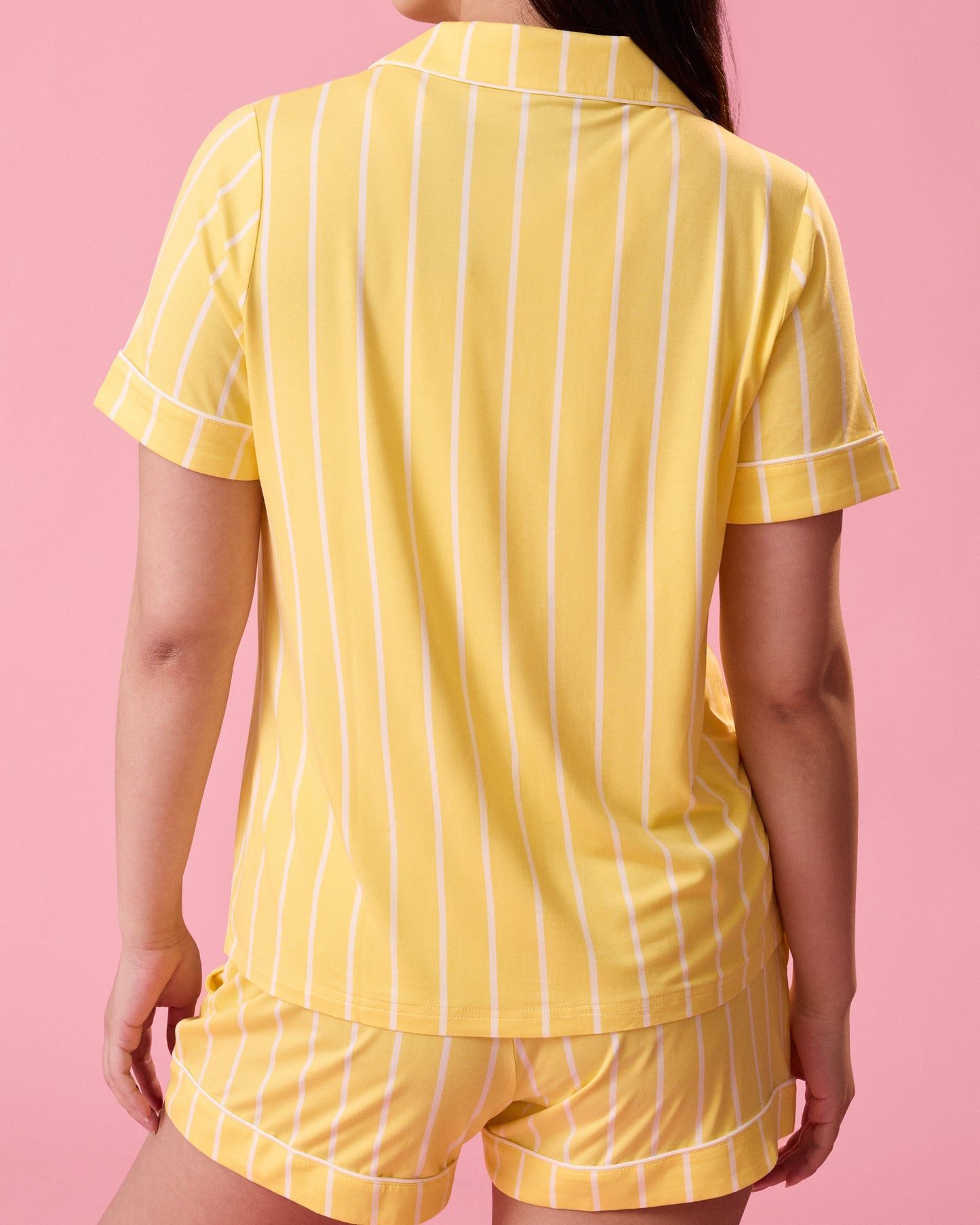 Back view of model wearing Clea Bamboo Short Sleeve Pajama Set in Dandelion Stripe on a pink background