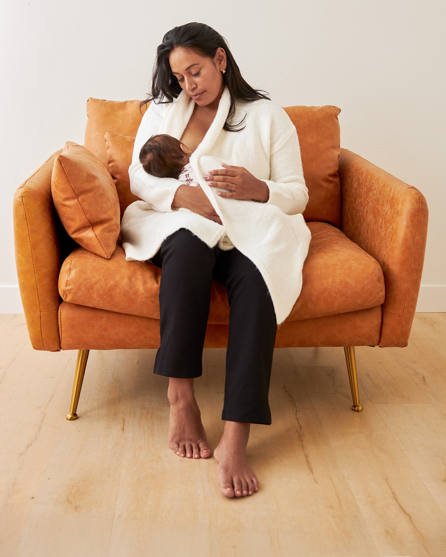Woman wearing the Chloe Cardigan Sweater in Ecru, sitting on chair and nursing baby@model_info:Lily is 5'5" and wearing a M/L.
