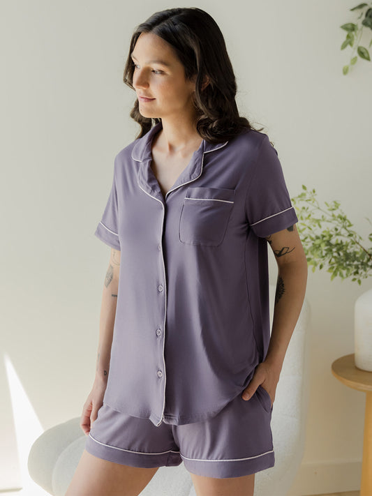 Model wearing the Clea Bamboo Short Sleeve Pajama Set in Granite, standing looking out window with one hand in pocket@model_info:Megan is wearing a Small.