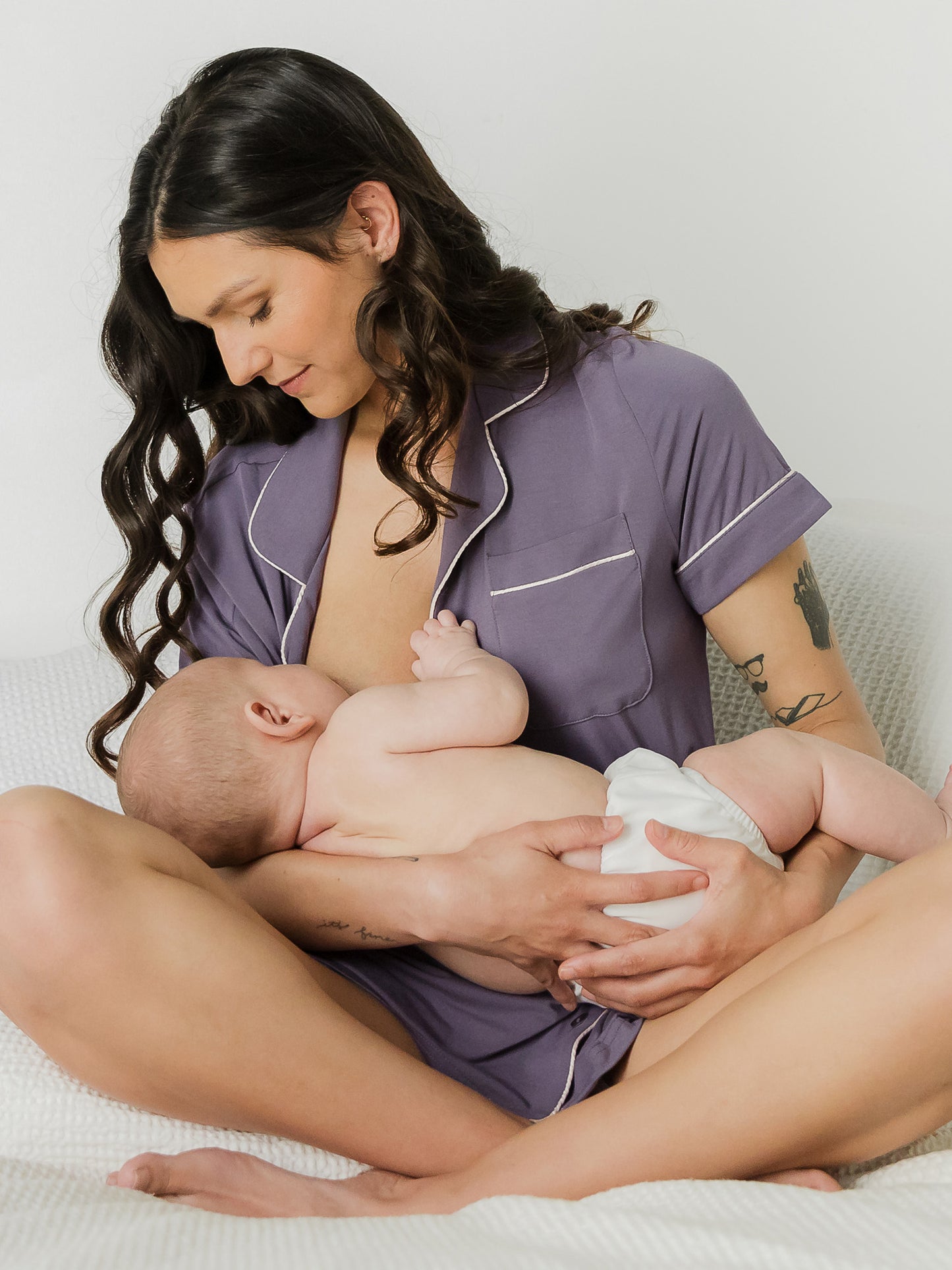 Model wearing the Clea Bamboo Short Sleeve Pajama Set in Granite, sitting cross-legged and nursing baby.