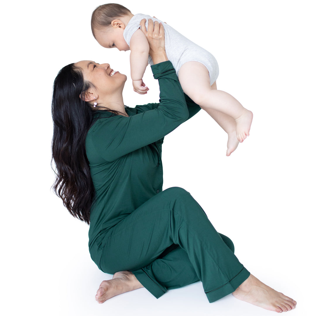 Model sitting while holding her baby up in the air wearing the Clea Bamboo Long Sleeve Pajama Set in Evergreen