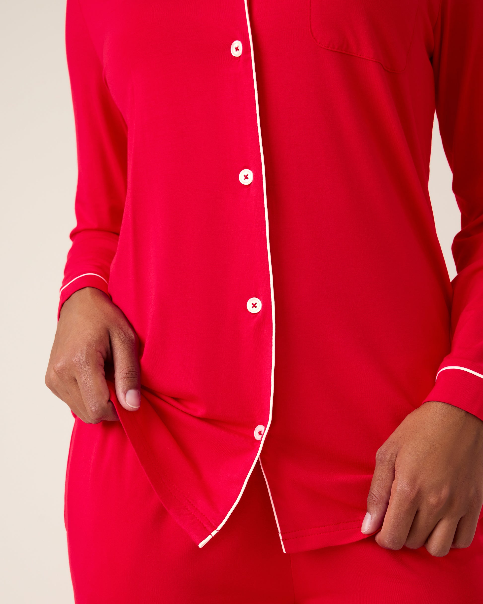 Woman wearing the Clea Bamboo Long Sleeve Pajama Set in Red, with white piping showing white buttons