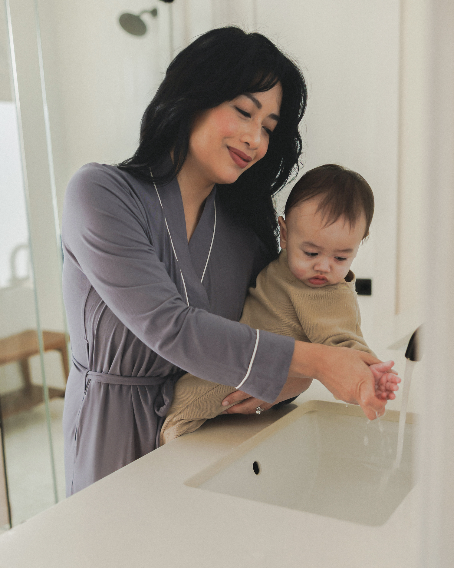 Model wearing the Clea Bamboo Robe in Granite while helping her baby rinse their hands 