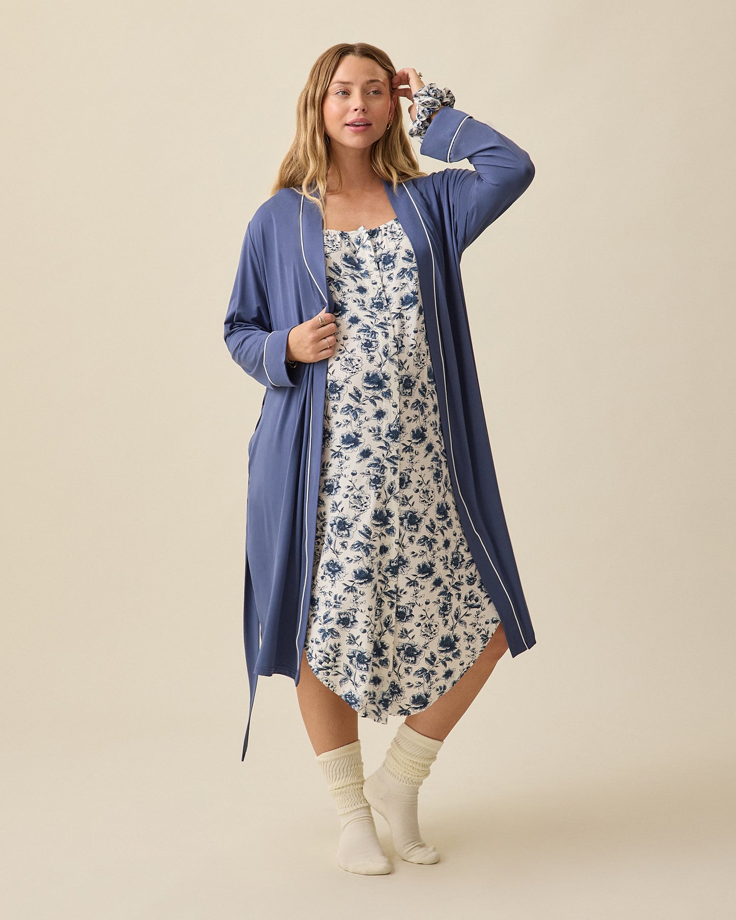 Model wearing Clea Robe in Slate Blue and Ruffle Strap Labor & Delivery Gown and Scrunchie in Navy Toile on a beige background.