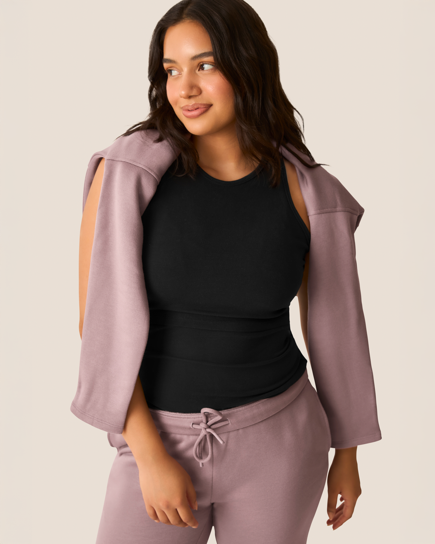 Woman wearing a black tank top and dusty mauve Cloud Fleece pants with a matching jacket on a beige background