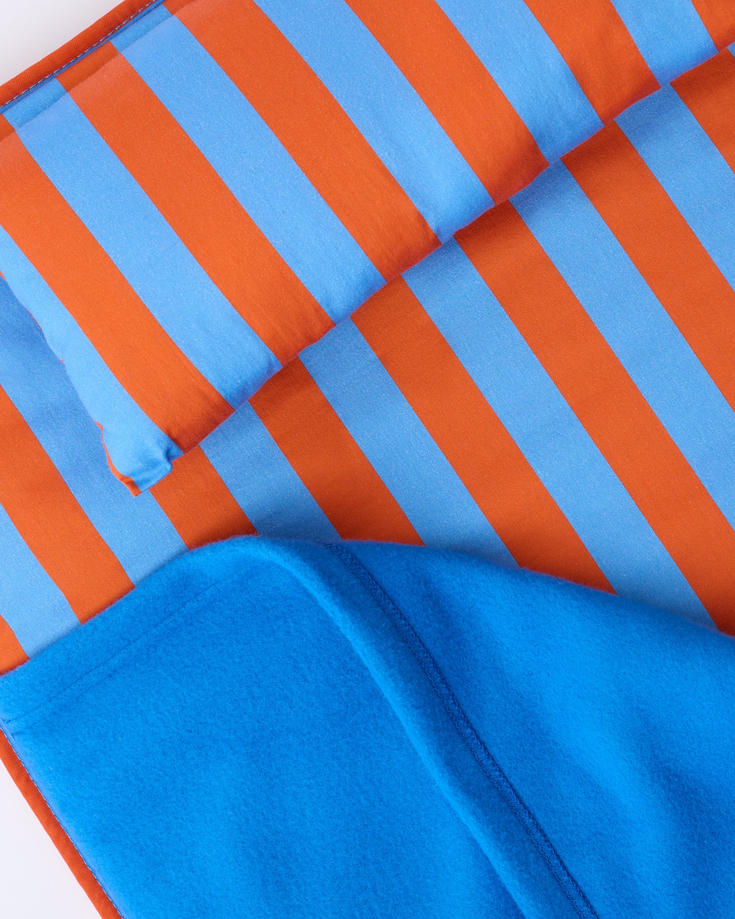 Close up image of the pillow and blanket of the Cool Kid Nap Mat in Blue & Rust Stripe on a beige background.