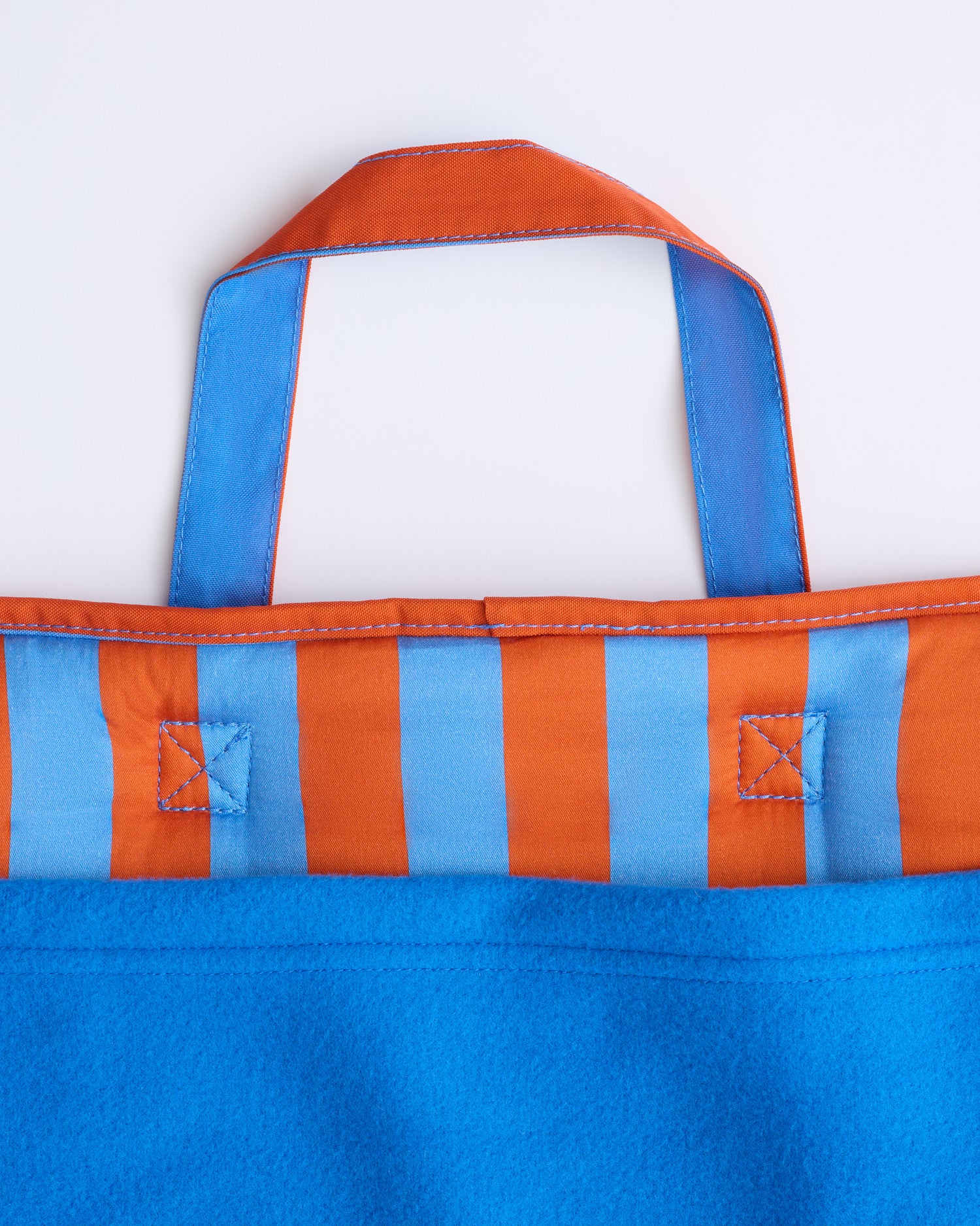 Close up image of the handle and blanket of the Cool Kid Nap Mat in Blue & Rust Stripe on a beige background.