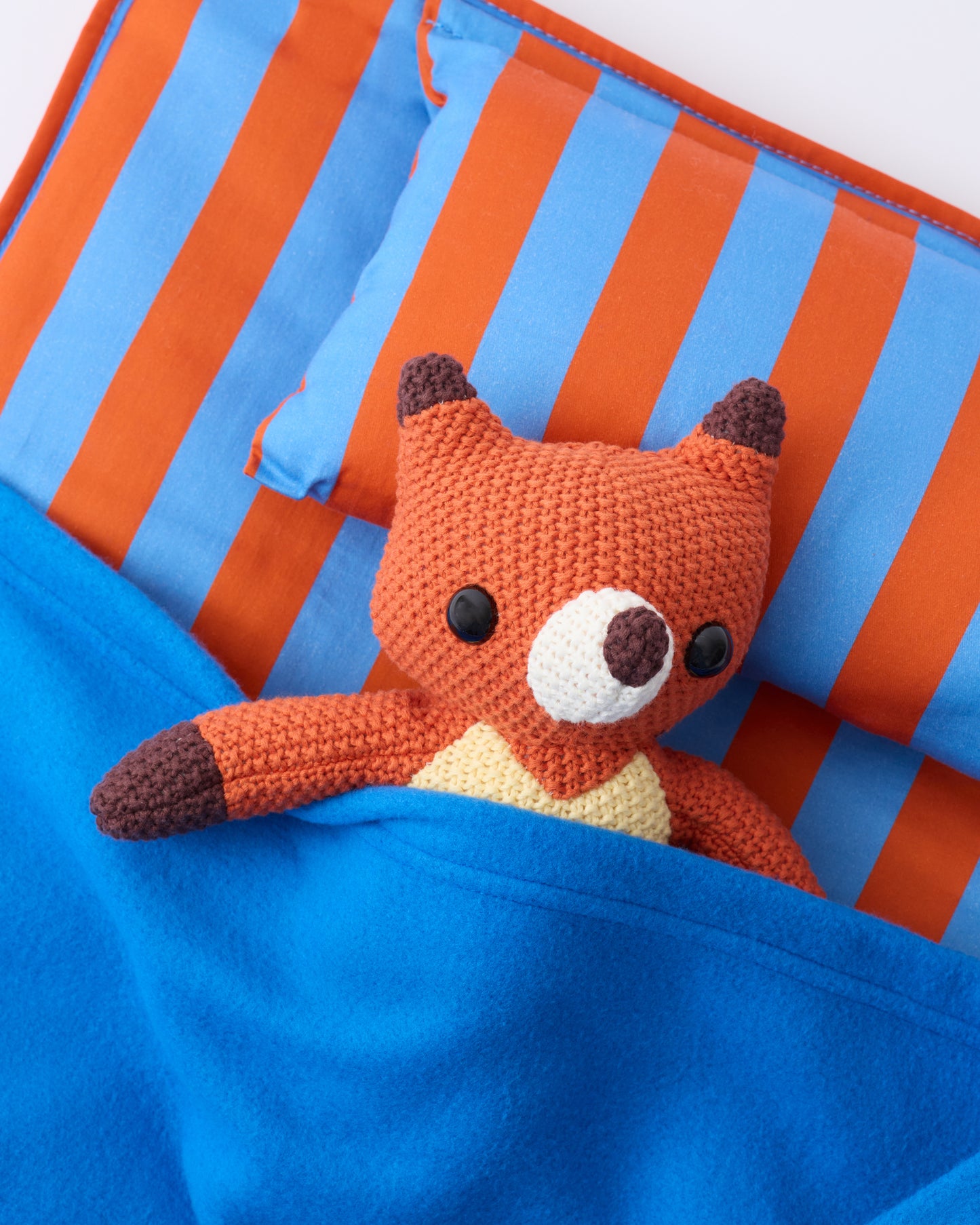 Close up image of the pillow and blanket of the Cool Kid Nap Mat in Blue & Rust Stripe with a little fox lovely resting on the pillow, on a beige background.