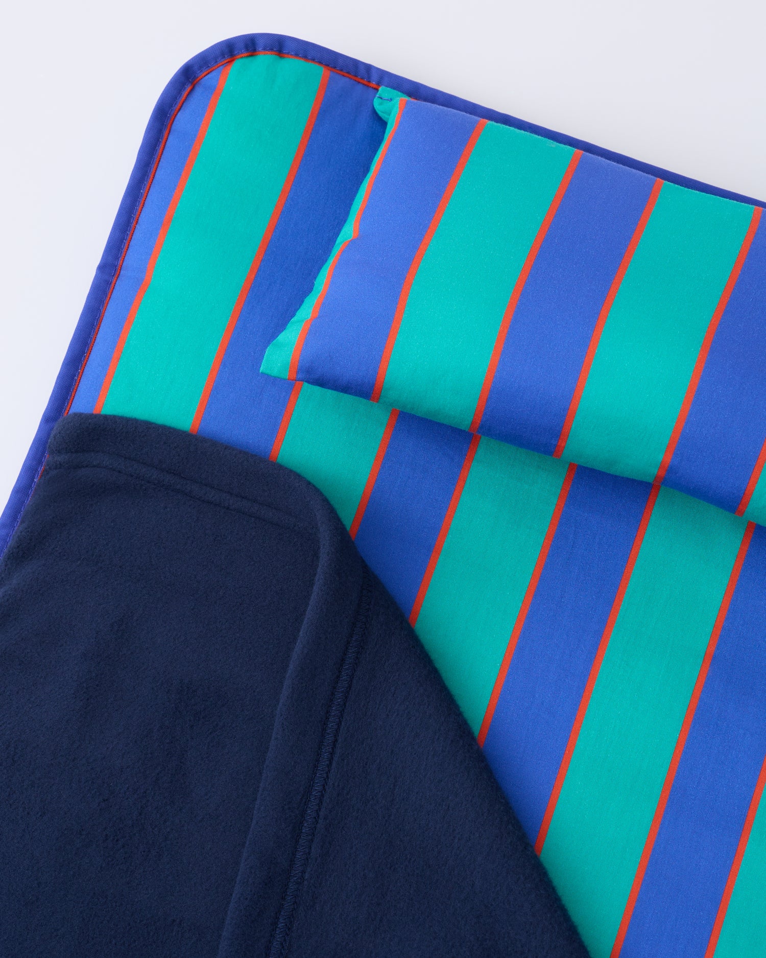 Close up of the pillow and blanket of the Cool Kid Nap Mat in Navy & Green Stripe on a beige background.