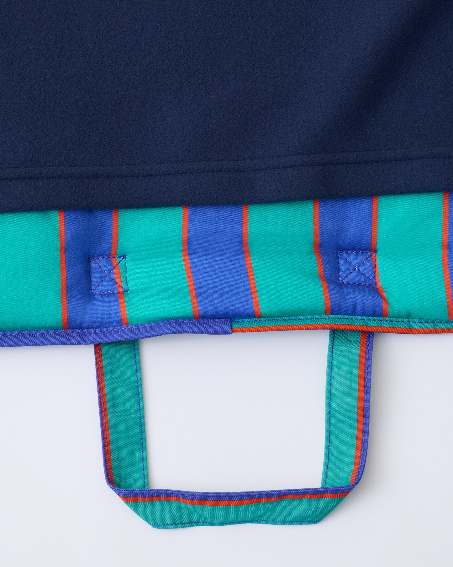 Close up of the handle and blanket of the Cool Kid Nap Mat in Navy & Green Stripe on a beige background.