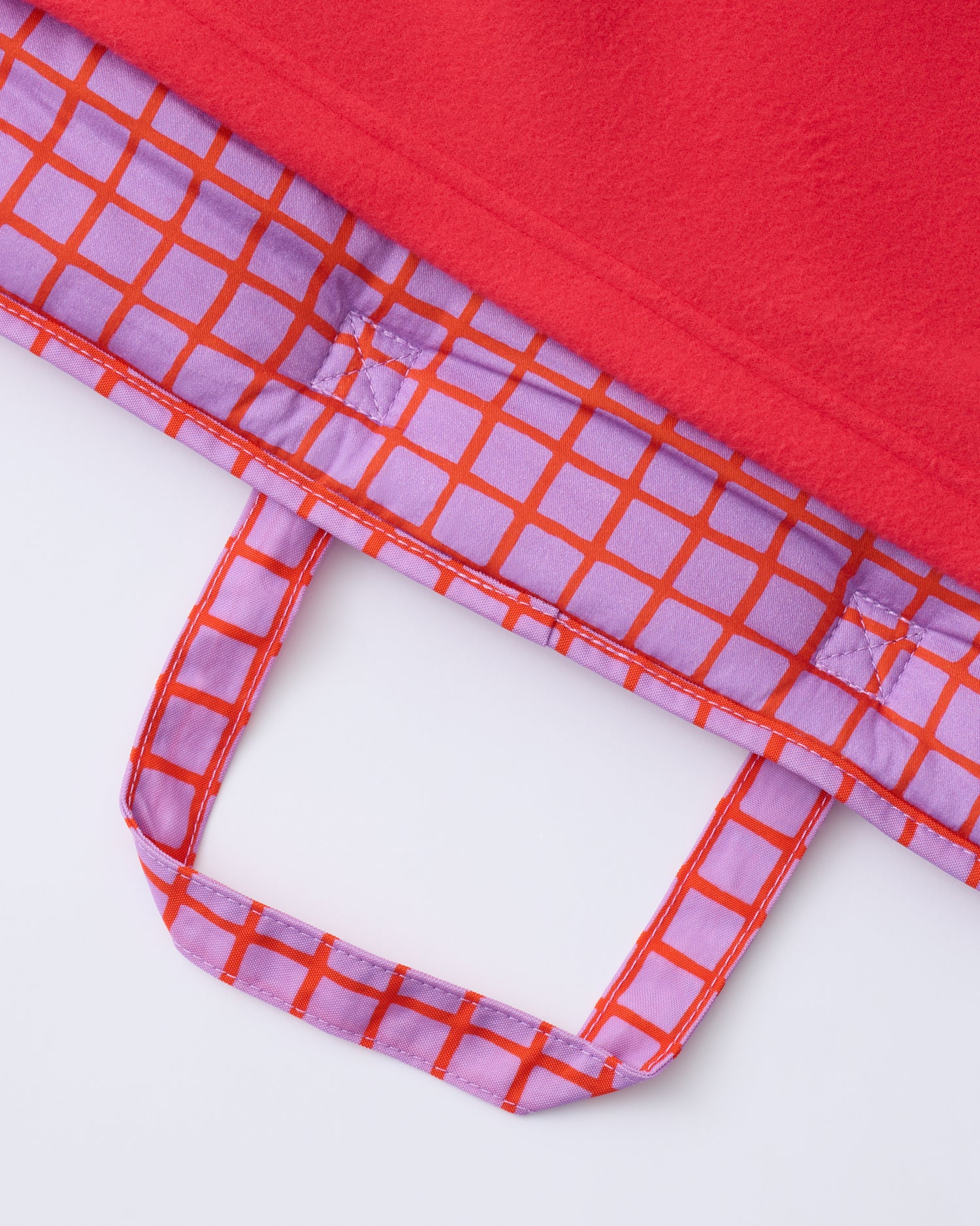 Close up of the handle and blanket of the Cool Kid Nap Mat in Orchid Grid on a beige background.