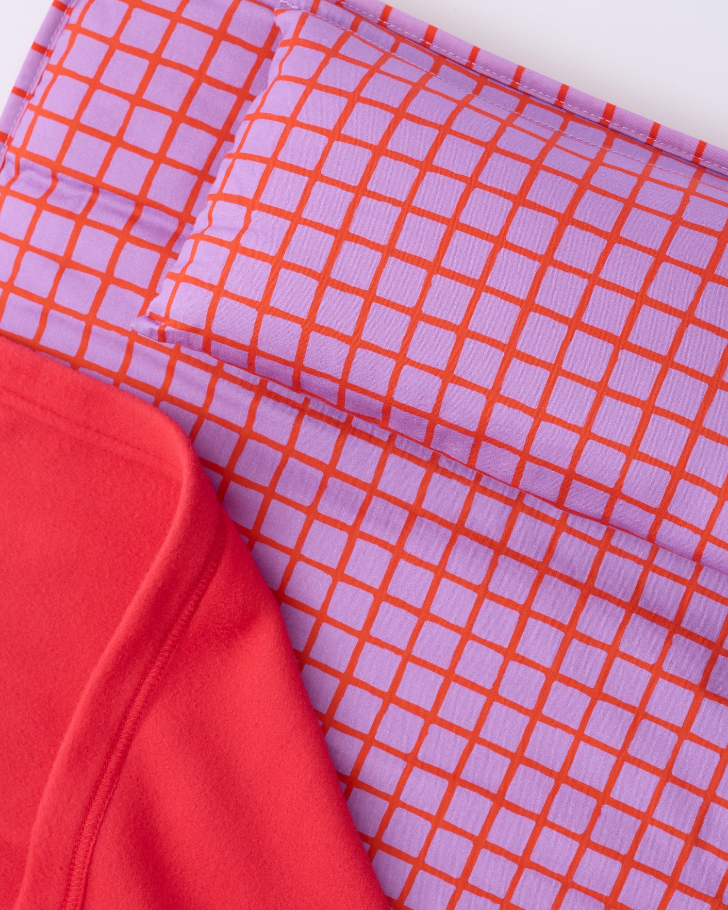 Close up of the pillow and blanket of the Cool Kid Nap Mat in Orchid Grid on a beige background.