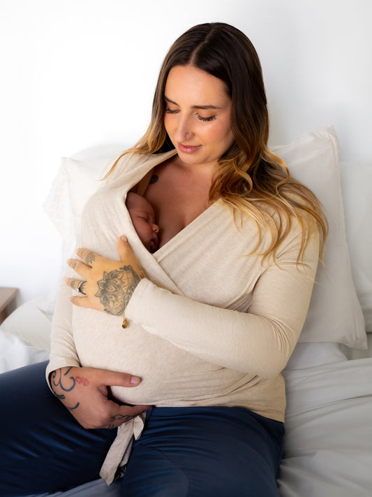 Model lounging and wearing the Organic Cotton Skin to Skin Long Sleeve Wrap Top in Oatmeal Heather, cradling baby who is wrapped in the top @model_info:Anna is wearing a Small.