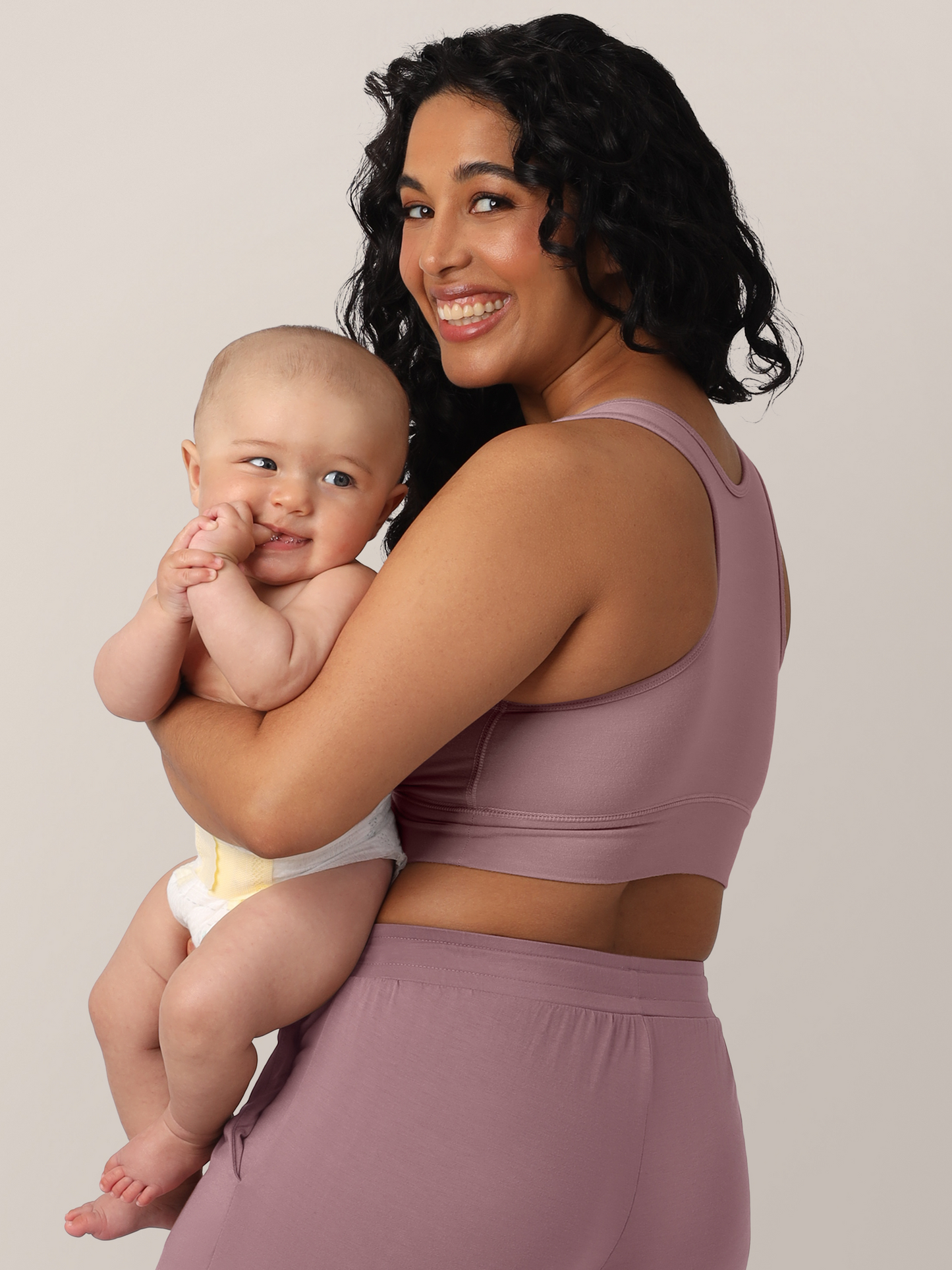 Side/ Back view of model wearing the French Terry Nursing Bra in Twilight and holding her smiling baby.
