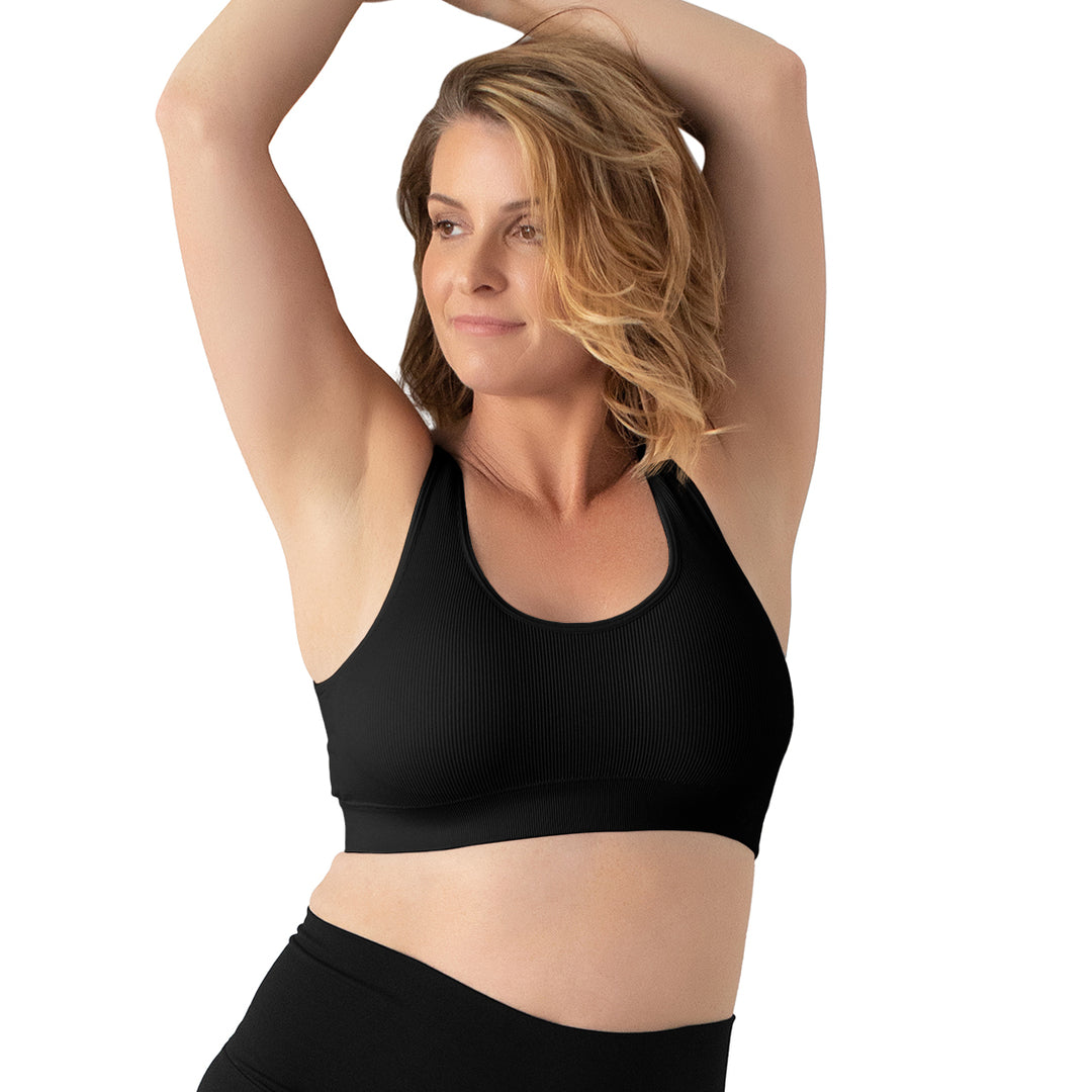 Model with her hands above her head wearing the Grace Ribbed Lounge Bra in Black. @model_info:Bethany is wearing a Medium.