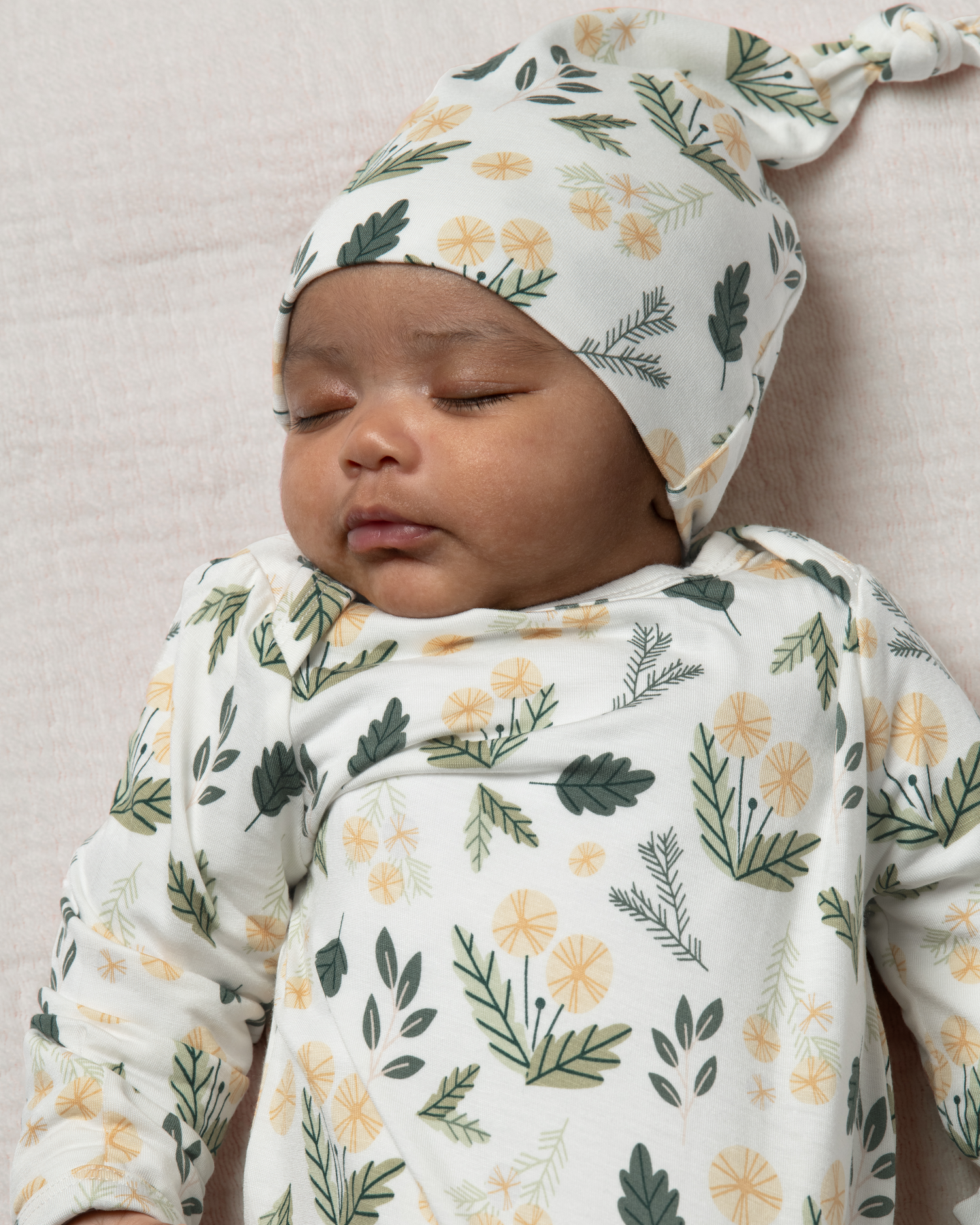 Baby wearing Bamboo Knotted Baby Gown in Honey Dandelion on a neutral background