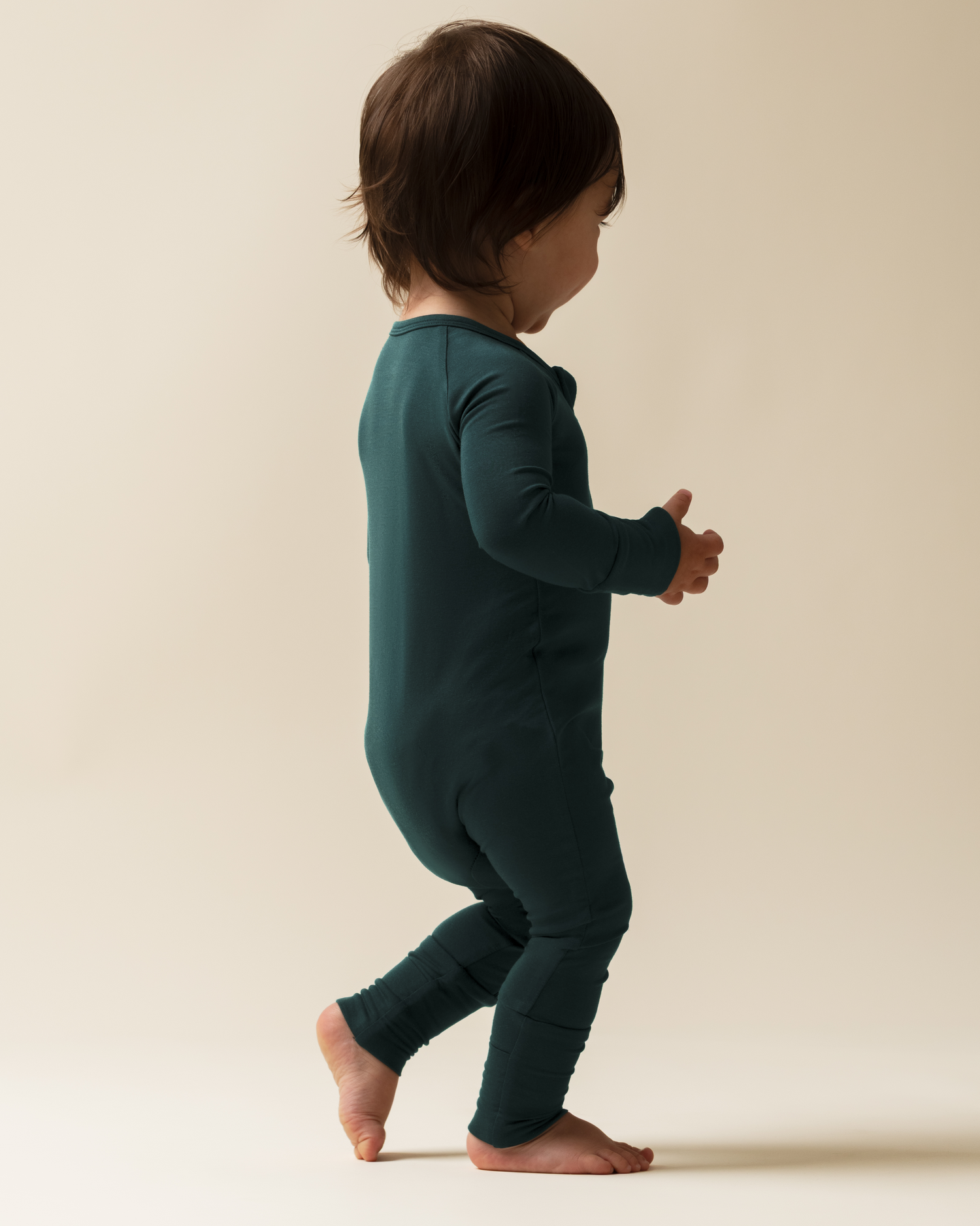 Child wearing Bamboo Baby Pajamas in Evergreen against a beige background