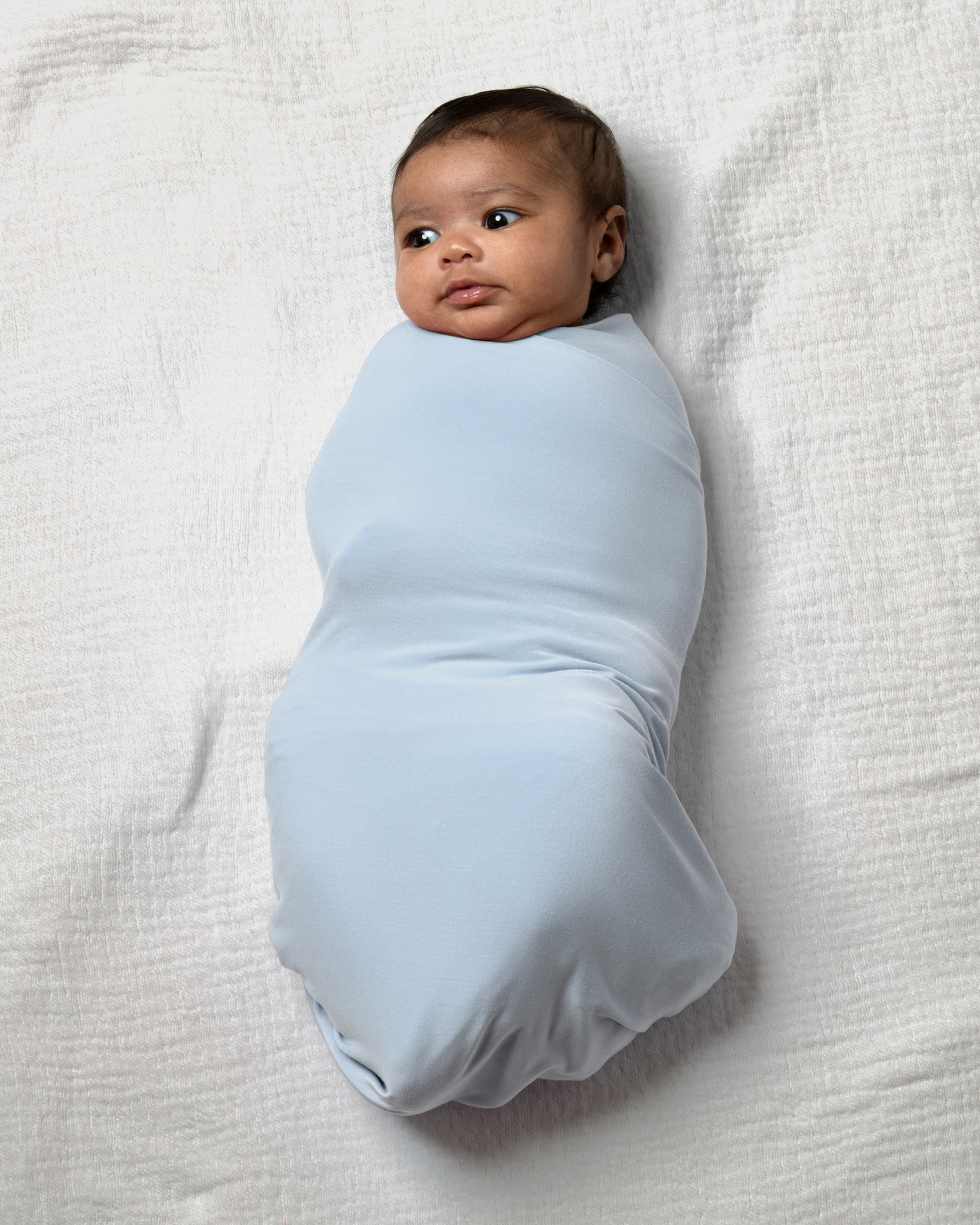 Baby wrapped in Bamboo Swaddle Blanket in French Blue on a white blanket@model_info:Luna is 6 weeks old.