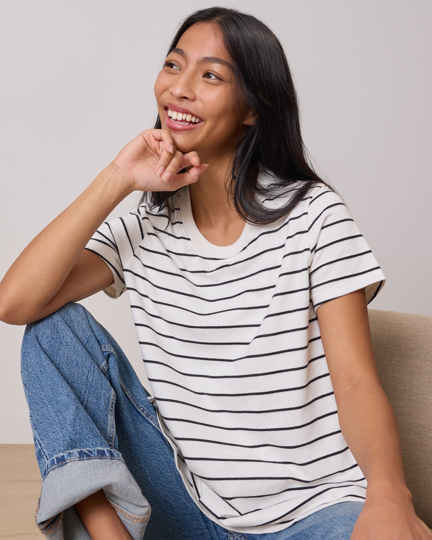 Model wearing Classic Cotton Nursing T-shirt in White & Black Stripe sitting on a lounging chair in a relaxed pose laughing